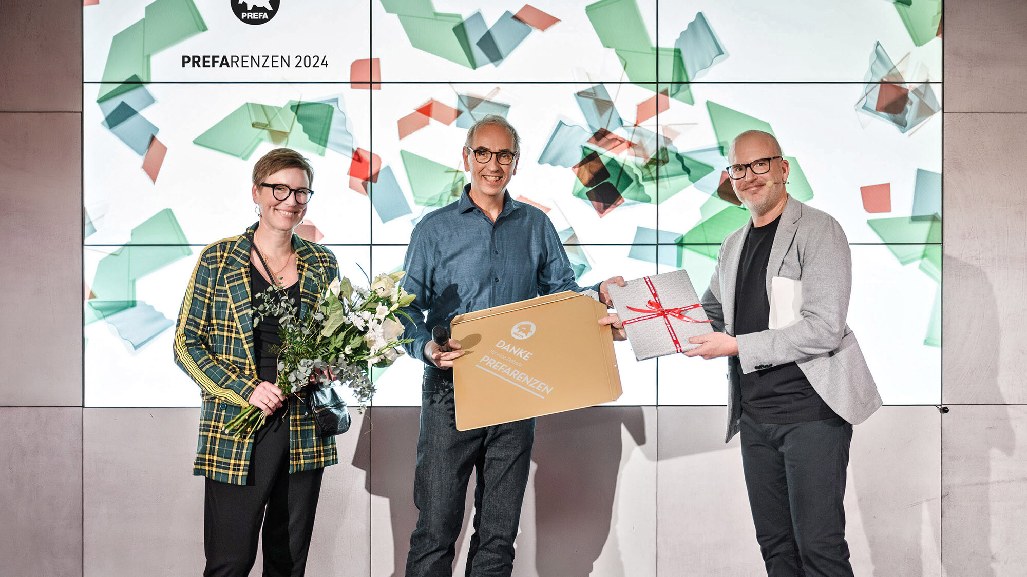 I fotografi Juliane Croce e Wolfgang Croce con il responsabile del marketing internazionale Jürgen Jungmair mentre ricevono un premio davanti all'area della presentazione.