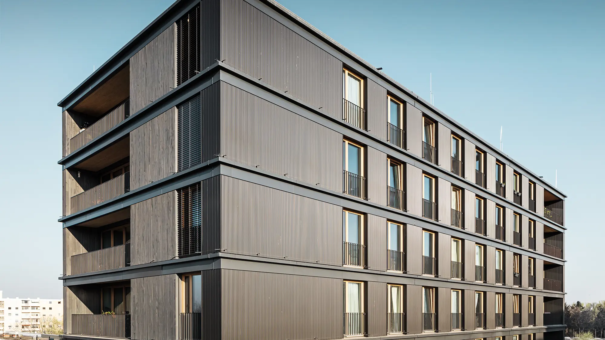 Vista laterale dell'edificio residenziale e commerciale: le differenze tra profilo ondulato di PREFA e la facciata in legno sono quasi impercettibili.