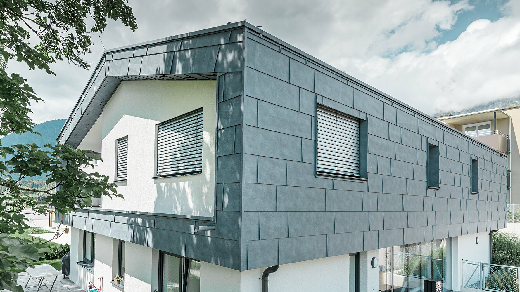 Einfamilienhaus mit dem PREFA Fassadenpaneel FX.12 in Steingrau Modernes Einfamilienhaus ohne Dachvorsprung; Die obere Etage wurde mit PREFA Fassadenpaneelen FX.12 in Steingrau verkleidet, der Rest der Fassade wurde weiß verputzt.