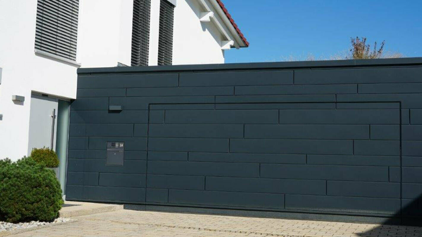 Facciata di un garage dopo la ristrutturazione con doghe di rivestimento PREFA color antracite, il portone è montato a filo della facciata