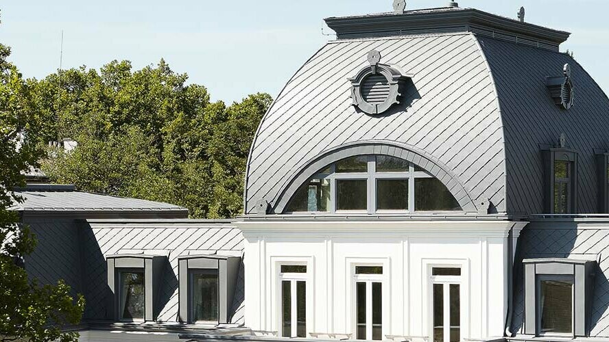 Il tetto a mansarda con cupola dell’edificio storico sotto tutela delle belle arti è stato ristrutturato con scaglie PREFA e Prefalz in P.10 grigio chiaro