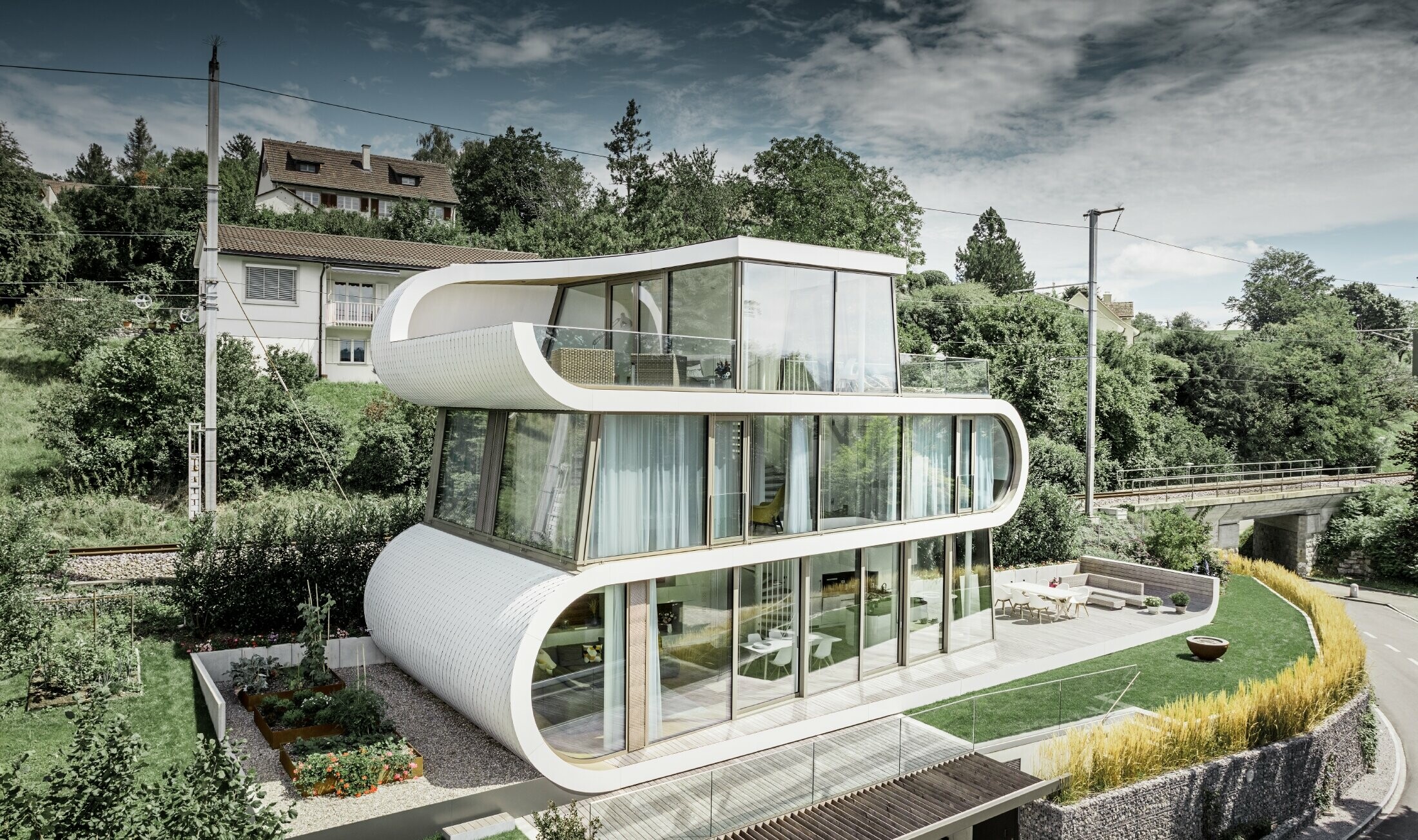 Modernissima casa unifamiliare progettata dall'architetto di Zurigo Camenzind; una fascia ricurva collega i singoli piani. Le curvature sono state rivestite con la scandola PREFA in bianco puro. La casa ha numerose ampie vetrate, che rendono l'intero ambiente particolarmente arioso.