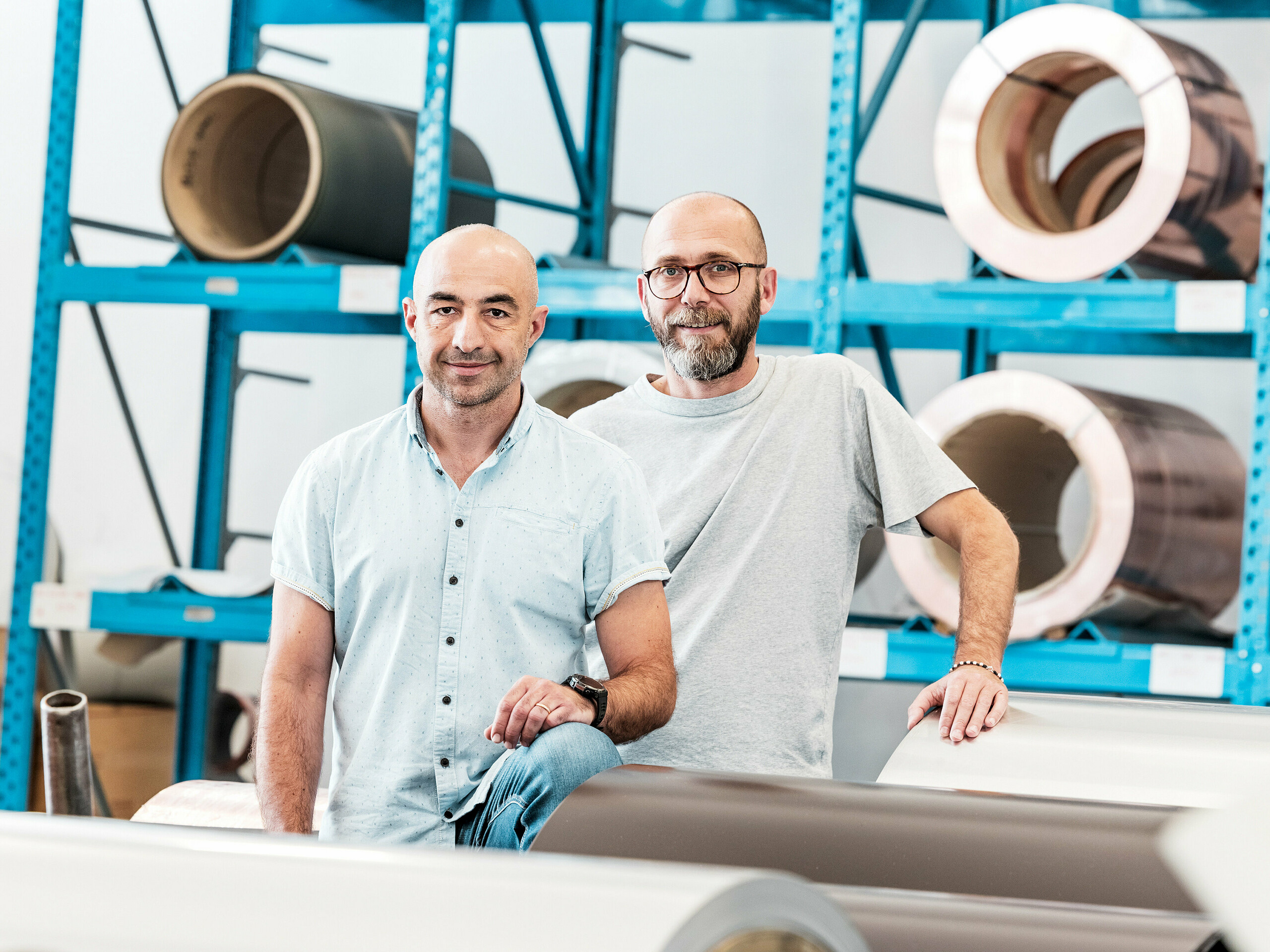 Zwei Handwerker im Aluminiumlager vor aufgewickelten Metallcoils – moderne Arbeitsumgebung für Dach- und Fassadensysteme aus Aluminium.