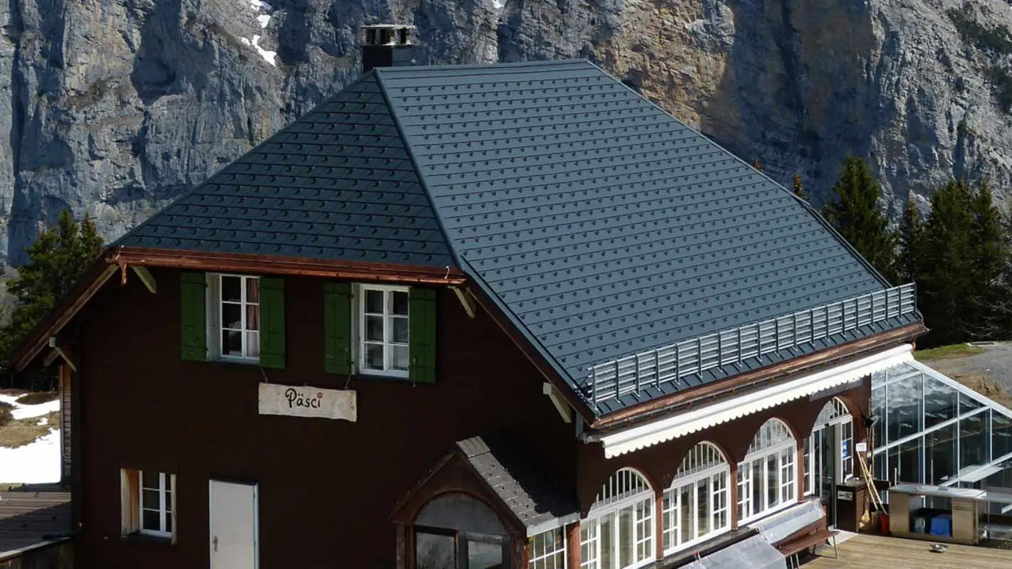 Ristrutturazione del tetto a due spioventi con falda a timpano di un rifugio di montagna con scandole PREFA e nasi paraneve