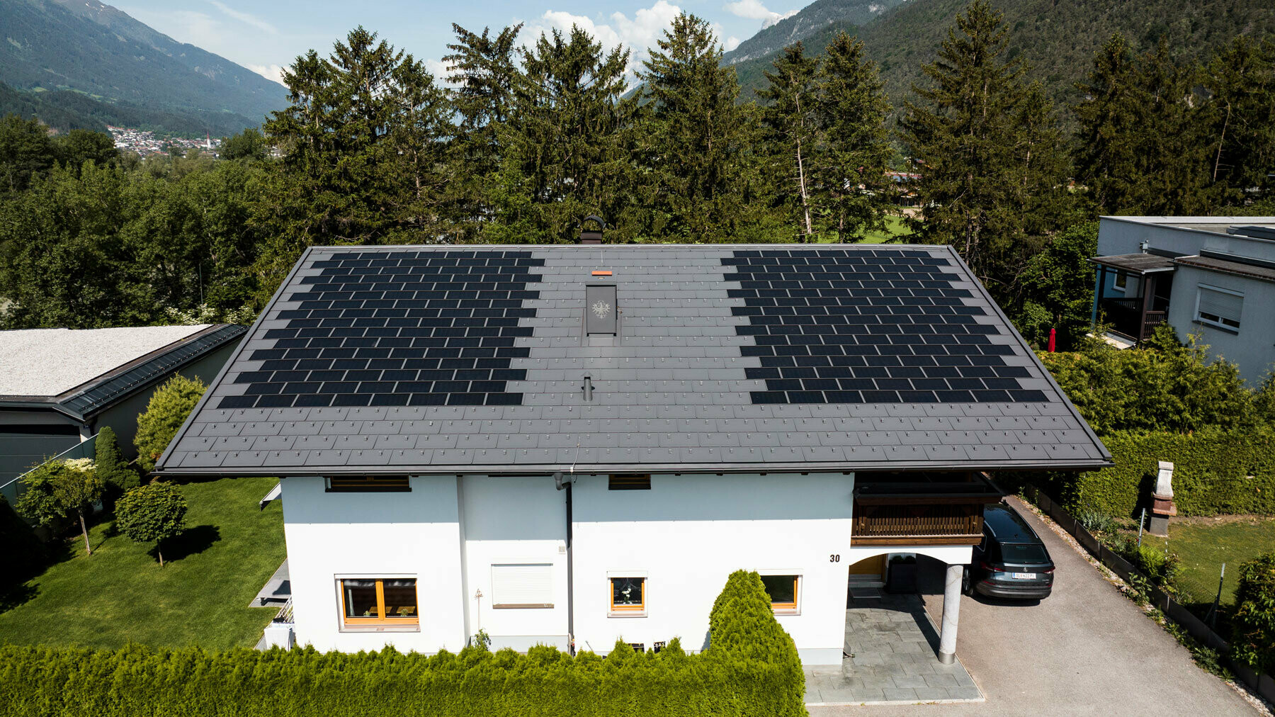 L'immagine mostra una casa unifamiliare coperta con la tegola fotovoltaica PREFA piccola e con la tegola R.16 nel colore P.10 grigio scuro in un ambiente rurale.