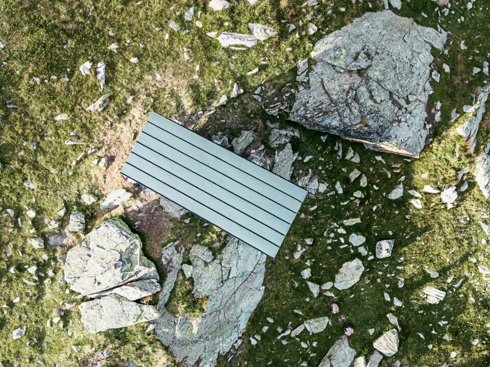 Das Brédy Biwak aus der Vogelperspektive, umgeben von Grünflächen und Gestein. Die anthrazifarbenen Aluminiumbahnen fügen sich optisch in die natürliche Umgebung ein.