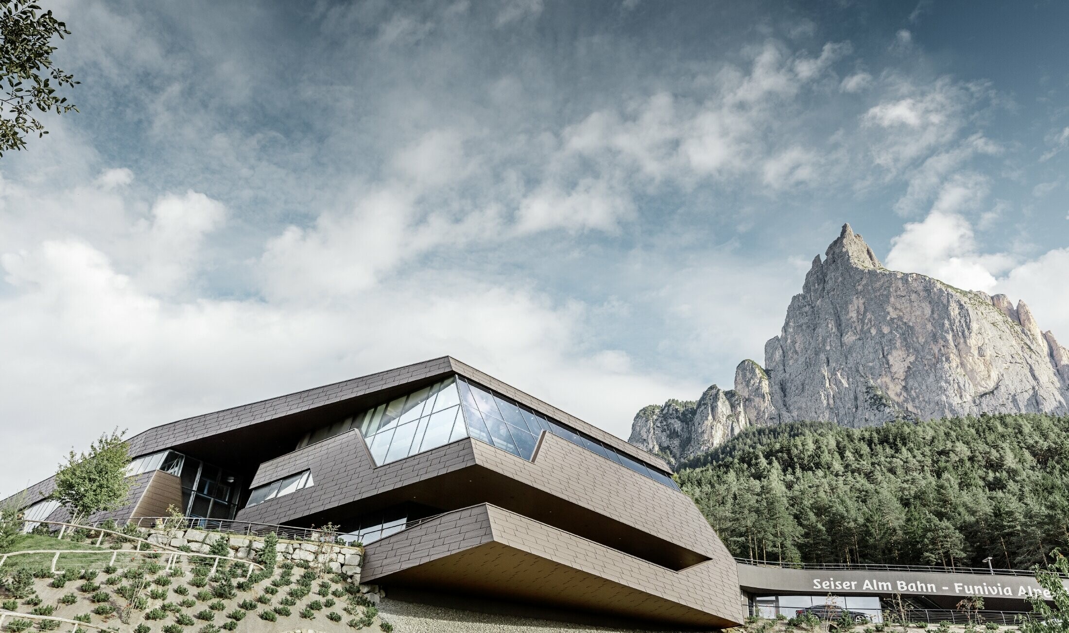 Stazione a valle della cabinovia dell'Alpe di Siusi, simile alle dolomiti sullo sfondo con bordi e superfici irregolari con una facciata in alluminio marrone di PREFA