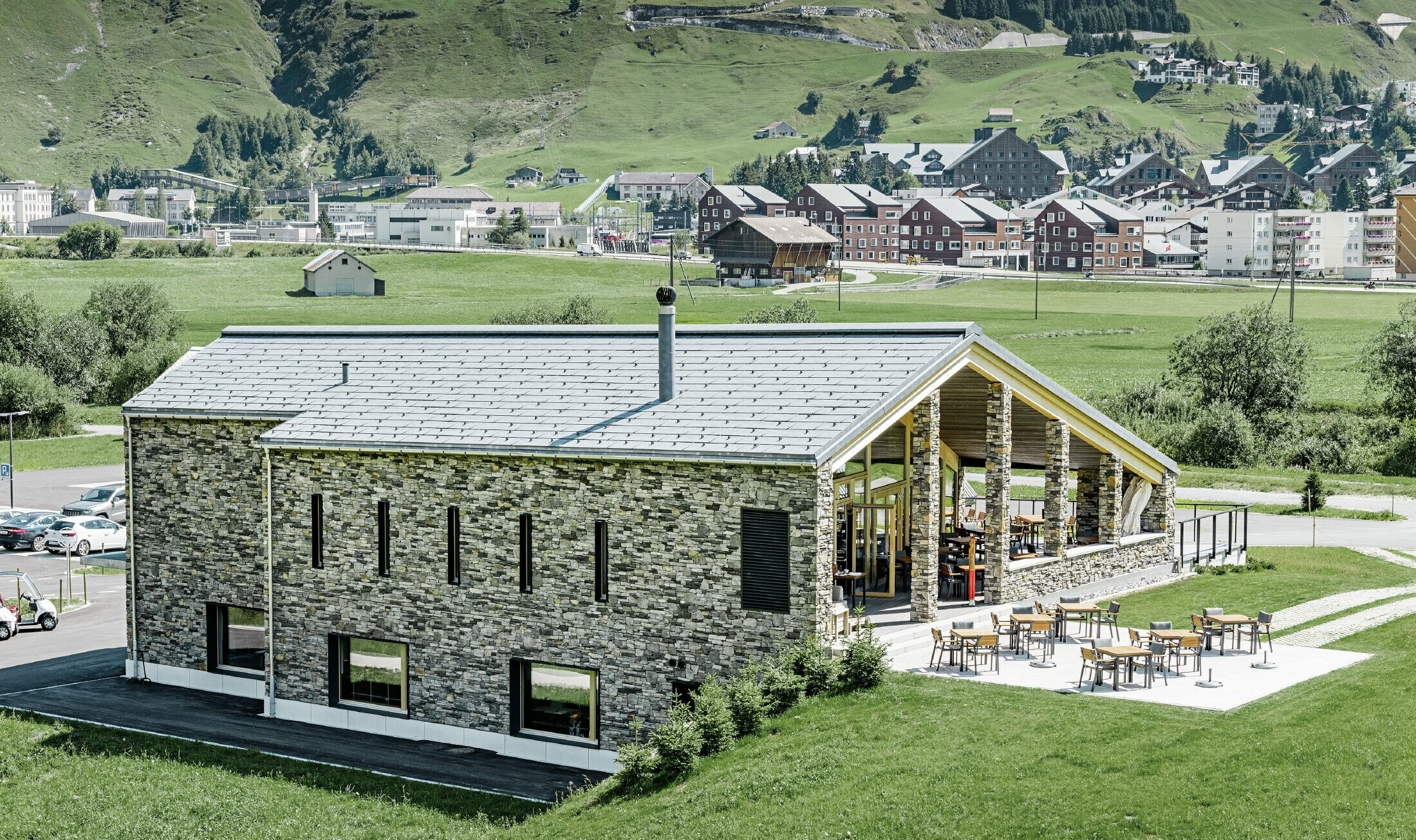 Il moderno punto di ritrovo del campo da golf a Andermatt con una facciata in pietra e il pannello per coperture FX.12 PREFA in alluminio in grigio pietra