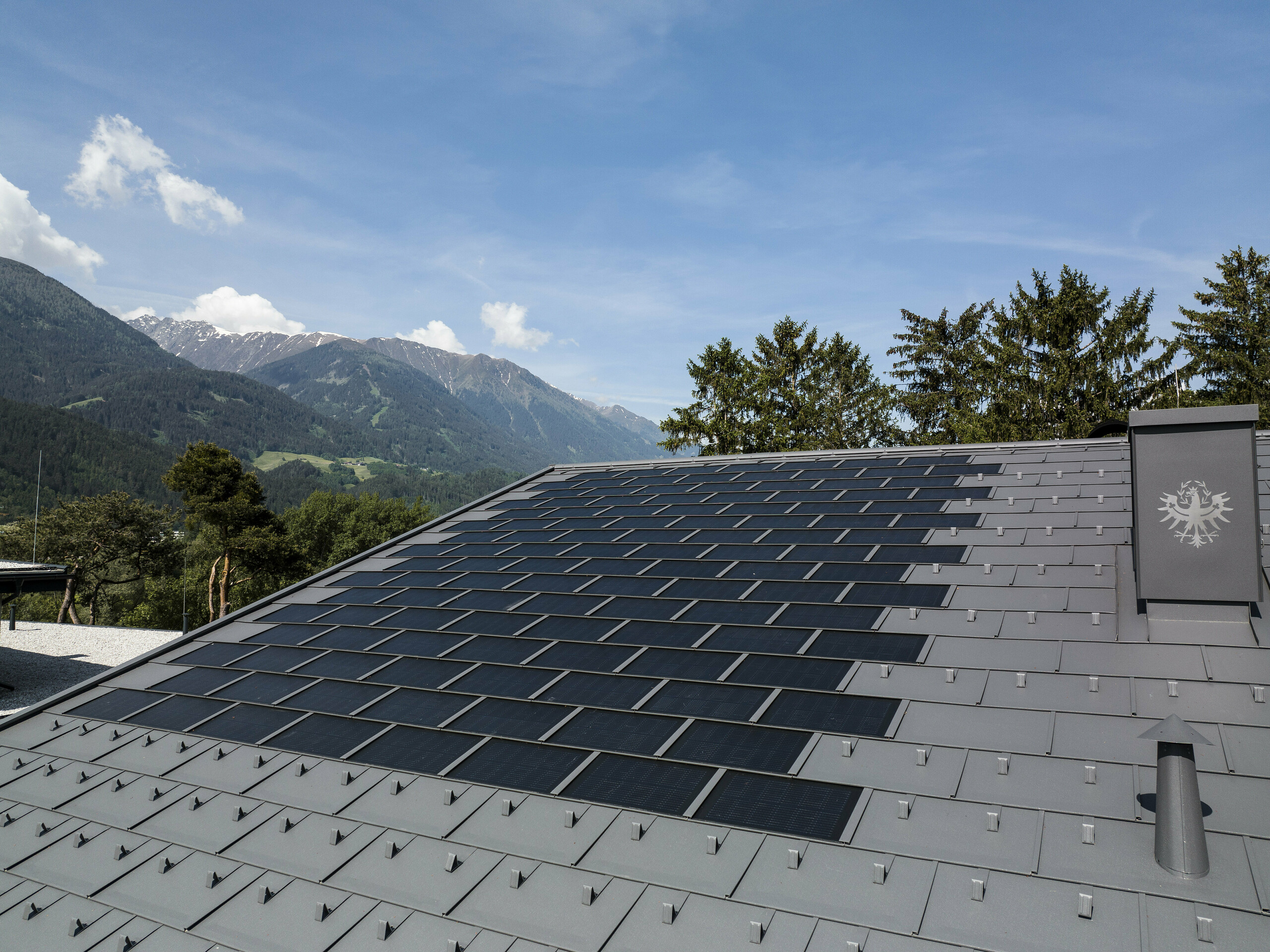 Una foto del tetto in Tirolo coperto con la tegola fotovoltaica PREFA R.16 nel colore P.10 grigio scuro.