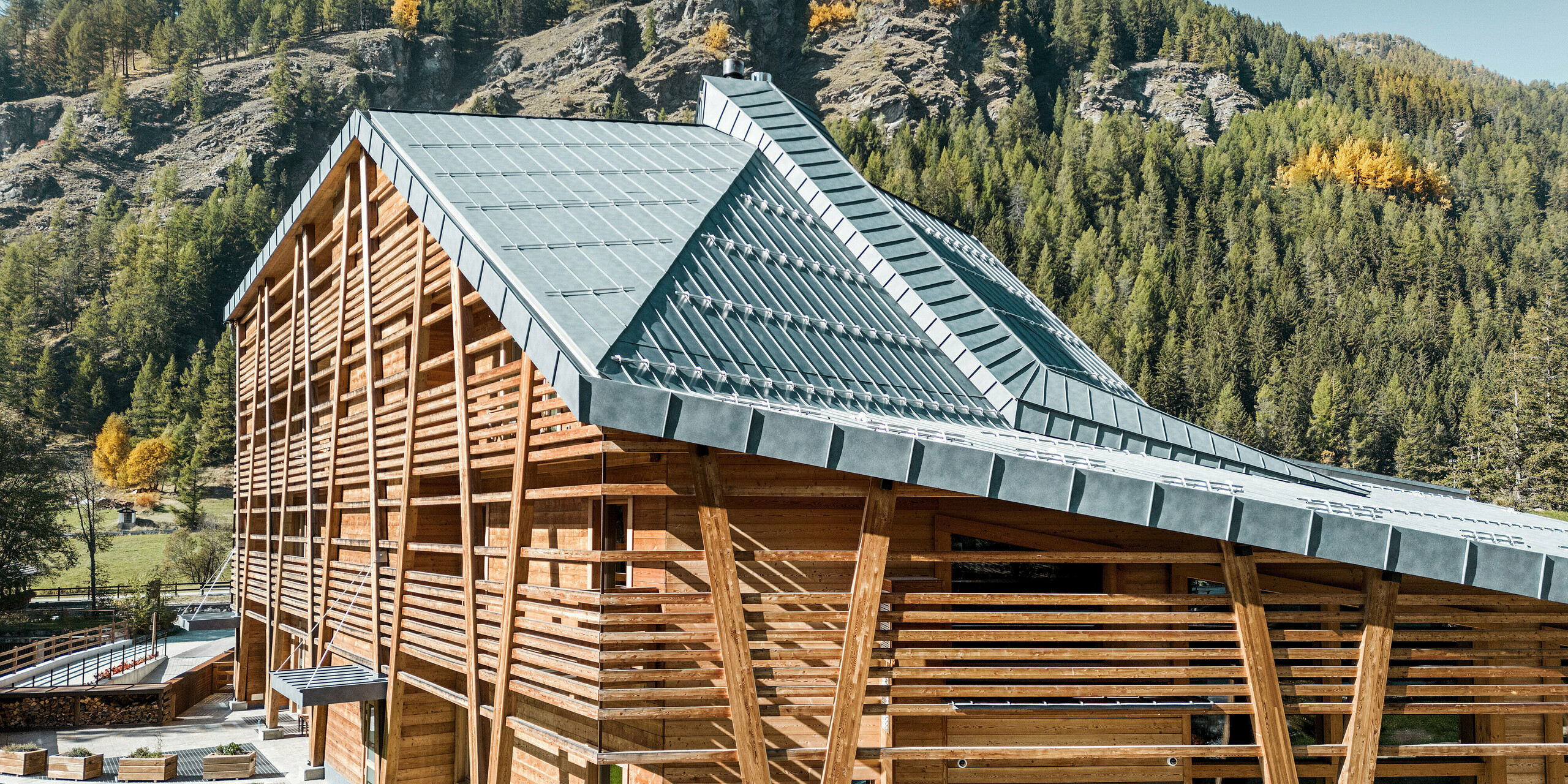 Das 5-Sterne-Öko-Hotel 'Au Charmant Petit Lac' in Champoluc, Italien, integriert sich mit seiner außergewöhnlichen Dachform und dem umgebenden Naturpanorama in eine malerische Landschaft. Das Dach, gedeckt mit PREFALZ in P.10 Steingrau, spiegelt die Farben der Natur wider und unterstreicht die Luxus-Ausrichtung des Hotels durch sein elegantes und nachhaltiges Design. Die Kombination aus natürlichem Holzbau und dem langlebigen PREFALZ Aluminium stellt eine Verbindung zwischen traditioneller Handwerkskunst und moderner Bautechnologie dar.