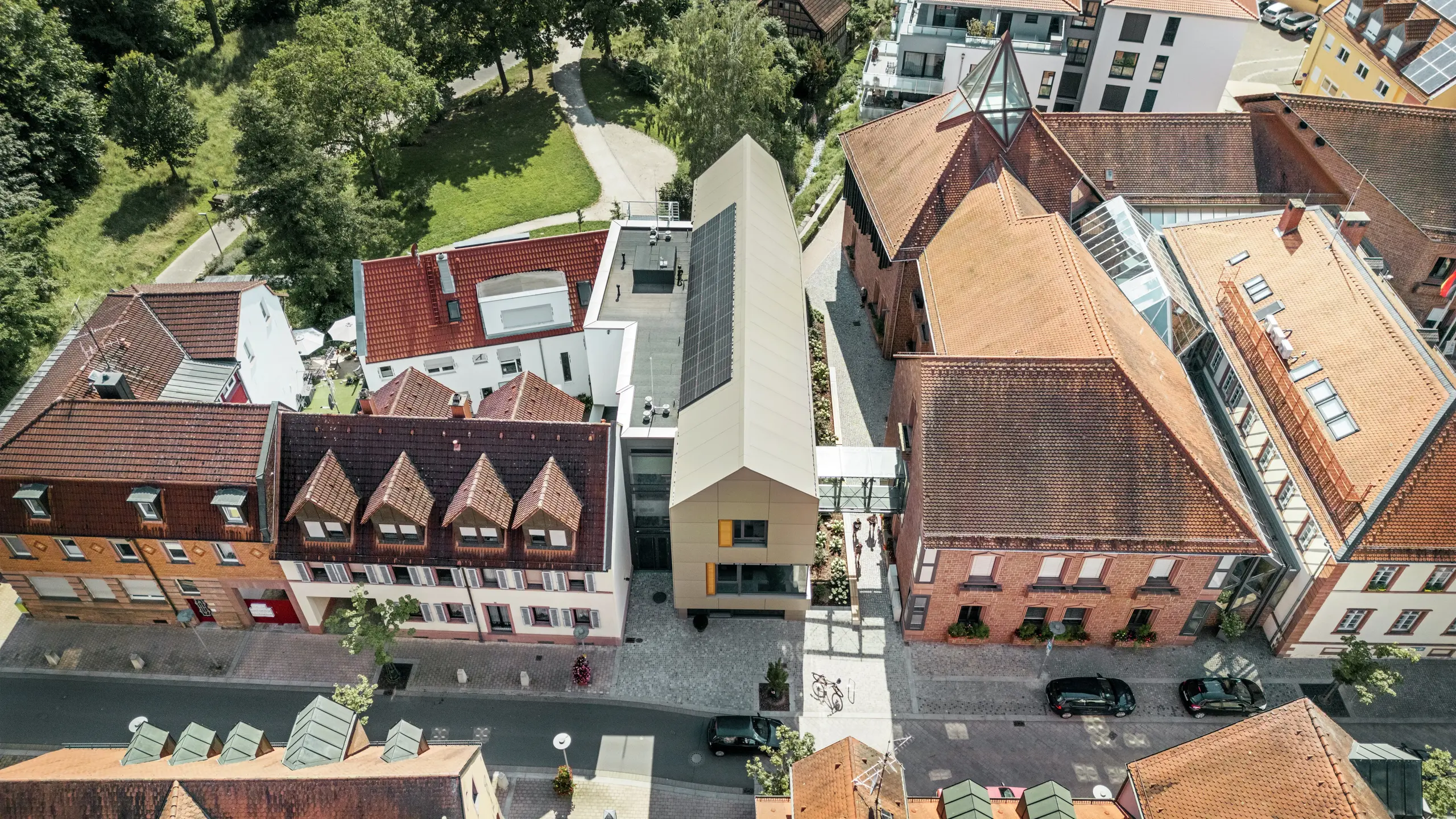 Il municipio di Alzenau, in Germania, si trova nel centro storico della città, circondato da edifici tradizionali con tetti di tegole rosse. In contrasto con questi ultimi, il moderno municipio presenta una facciata rivestita con pannelli compositi in alluminio PREFA in un'elegante tonalità bronzo. L'architettura innovativa si distingue chiaramente dagli edifici classici circostanti, integrandosi tuttavia armoniosamente nel paesaggio urbano.