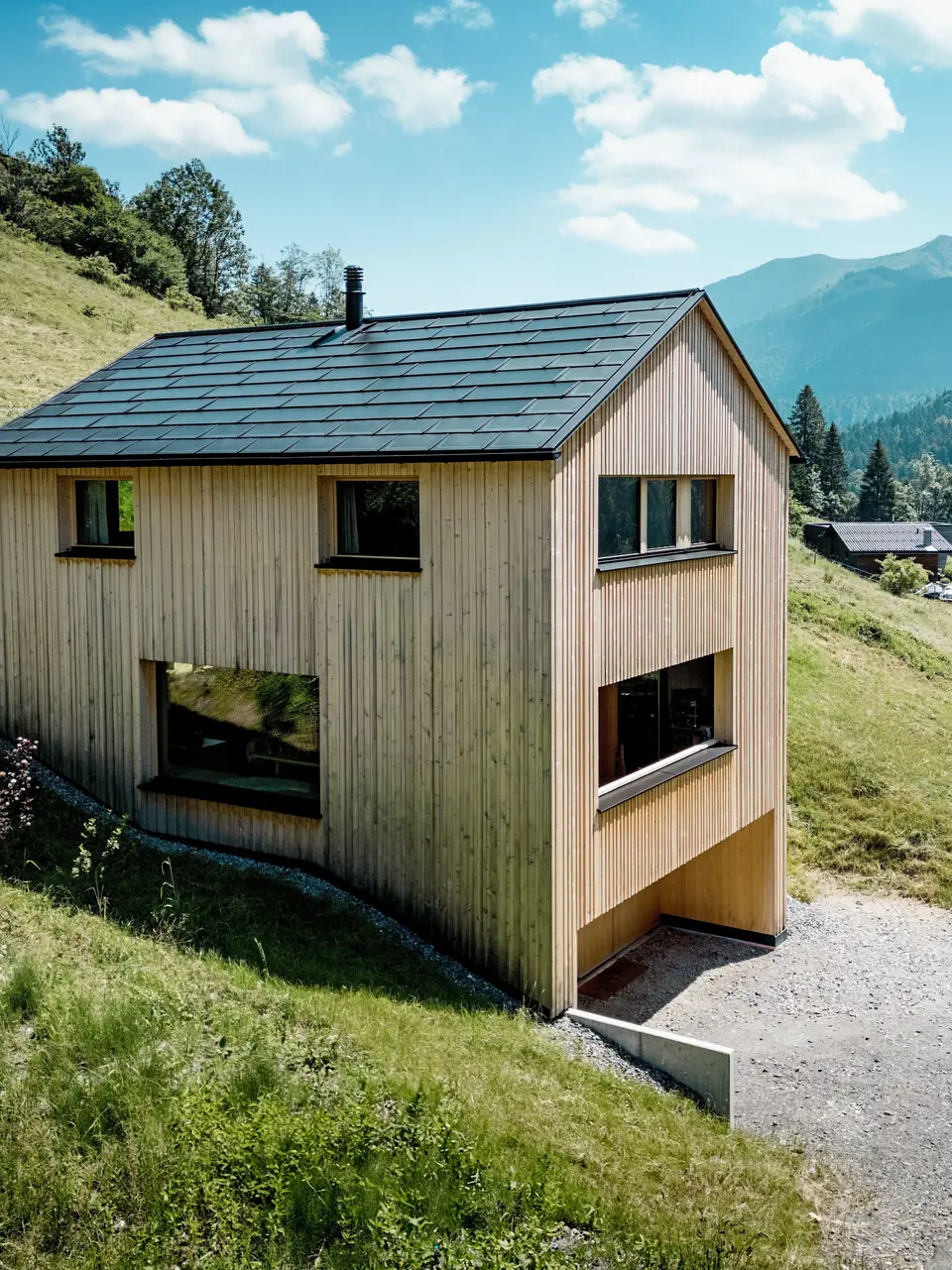 In alto sopra la valle, la casa Immi si erge come un monolite di legno dalle linee pulite sul soleggiato versante montuoso di Ebnit. La facciata essenziale in abete bianco e il tetto solare nero PREFA creano un forte contrasto con l’ampio paesaggio alpino. Le tegole fotovoltaiche integrate nel tetto e le tegole R.16 in P.10 nero forniscono energia elettrica, resistono alle intemperie alpine e garantiscono un aspetto armonioso e duraturo del tetto.