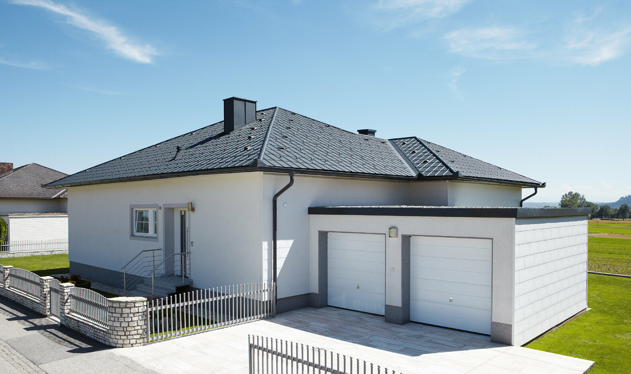 Il bungalow di nuova costruzione con tetto a tenda è stato coperto con le Tegole PREFA in P.10 antracite. A destra è stato aggiunto un garage doppio, la foto è stata scattata dalla strada.