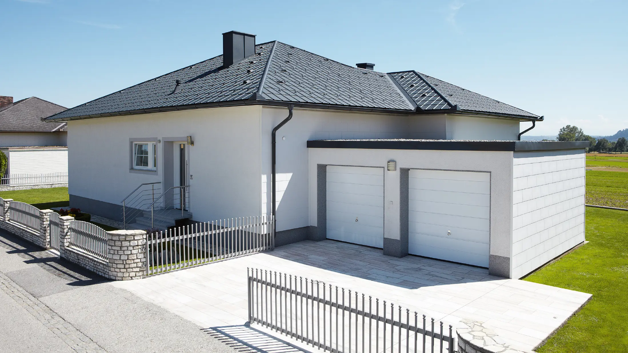 Il bungalow di nuova costruzione con tetto a tenda è stato coperto con le Tegole PREFA in P.10 antracite. A destra è stato aggiunto un garage doppio, la foto è stata scattata dalla strada.