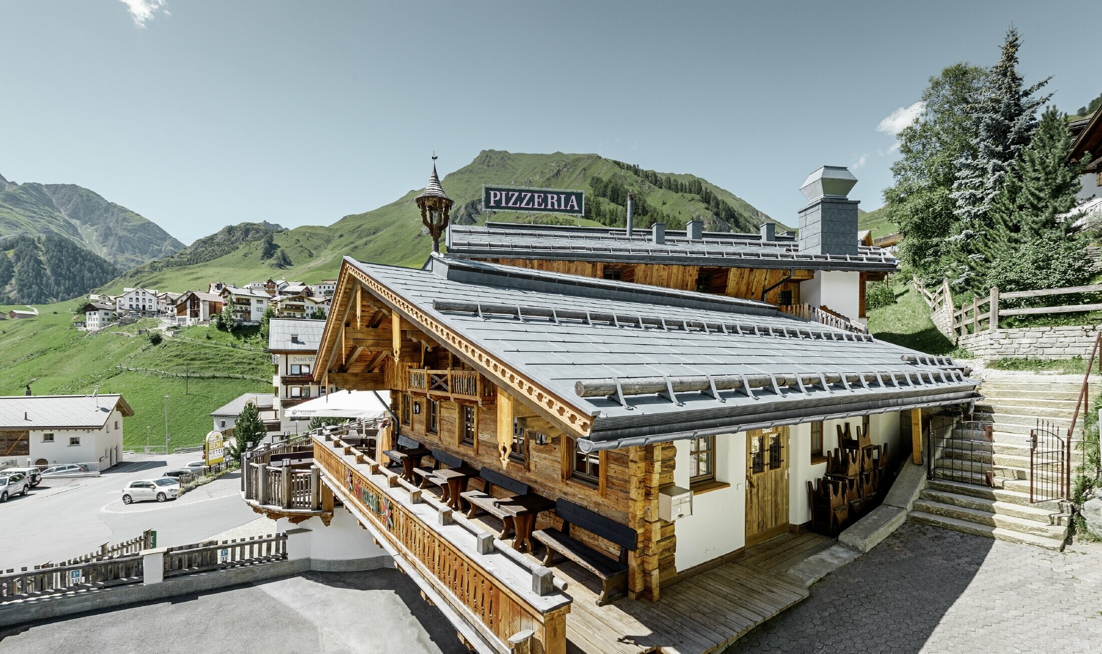 Ristorante Almrausch con montagne sullo sfondo e una copertura PREFA con il pannello per coperture FX.12 in grigio pietra e fermaneve