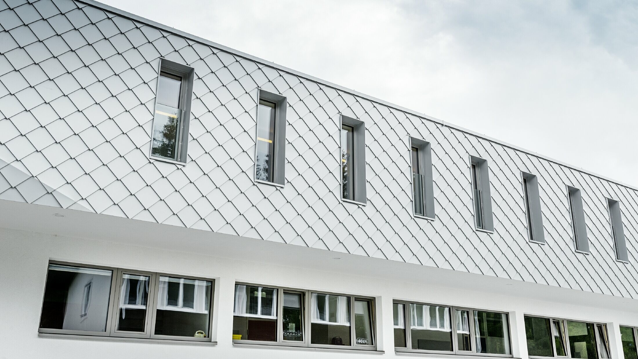 Scuola materna di nuova costruzione a Kaprun con una moderna facciata in alluminio con la scaglia per facciata PREFA in bianco PREFA