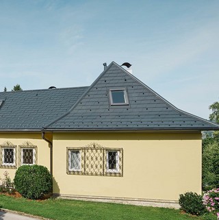 Einfamilienhaus mit Walmdach und mit gelber Putzfassade; Das Dach wurde mit der PREFA Dachschindel in Anthrazit eingedeckt.