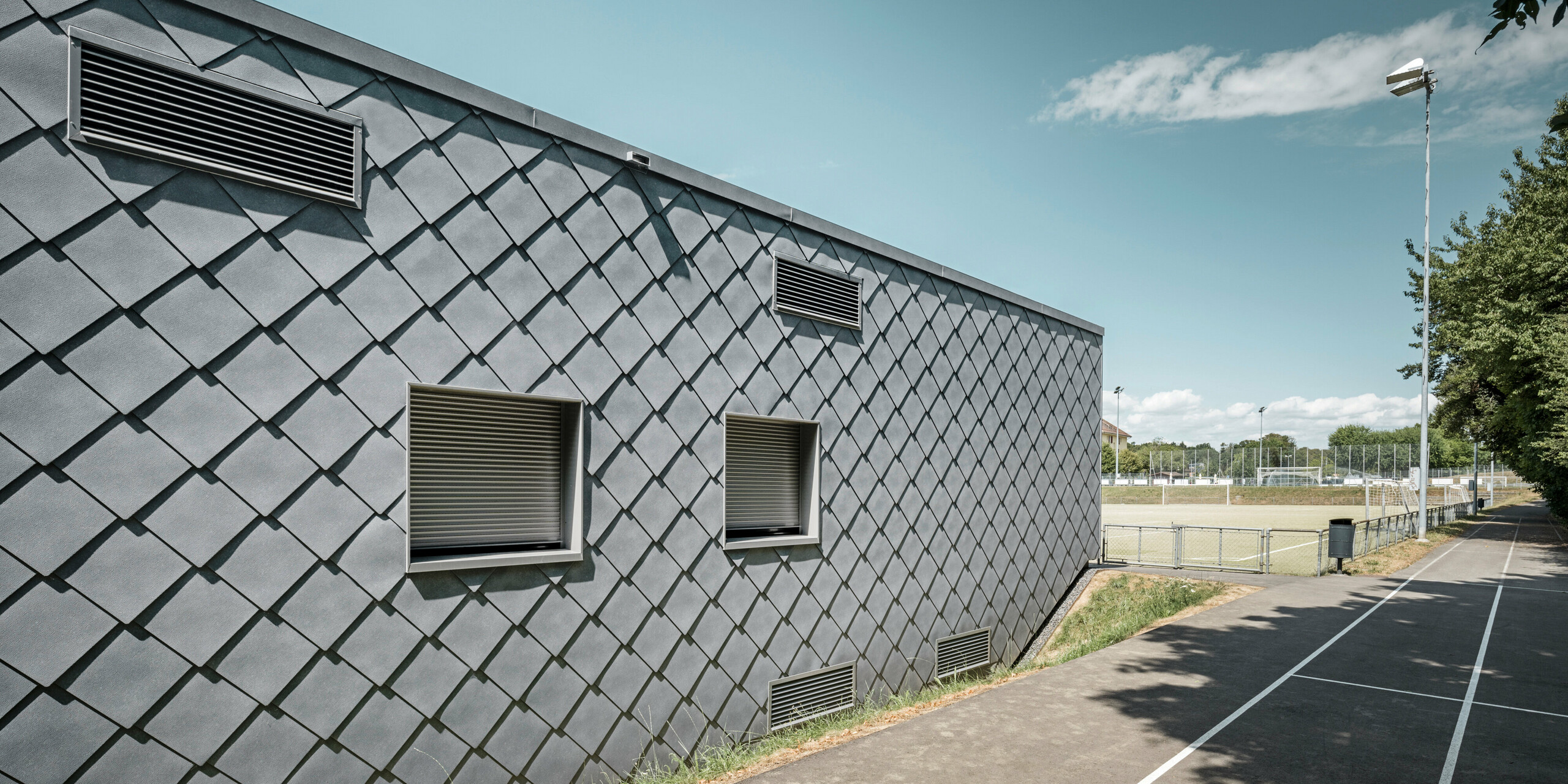 Das Gebäude einer Sportanlage in Prilly in der Schweiz wurde mit der PREFA Dach- und Wandraute 44x44 in P.10 Steingrau verkleidet. Auf dem Dach wurde großflächig eine Photovoltaikanlage montiert. 