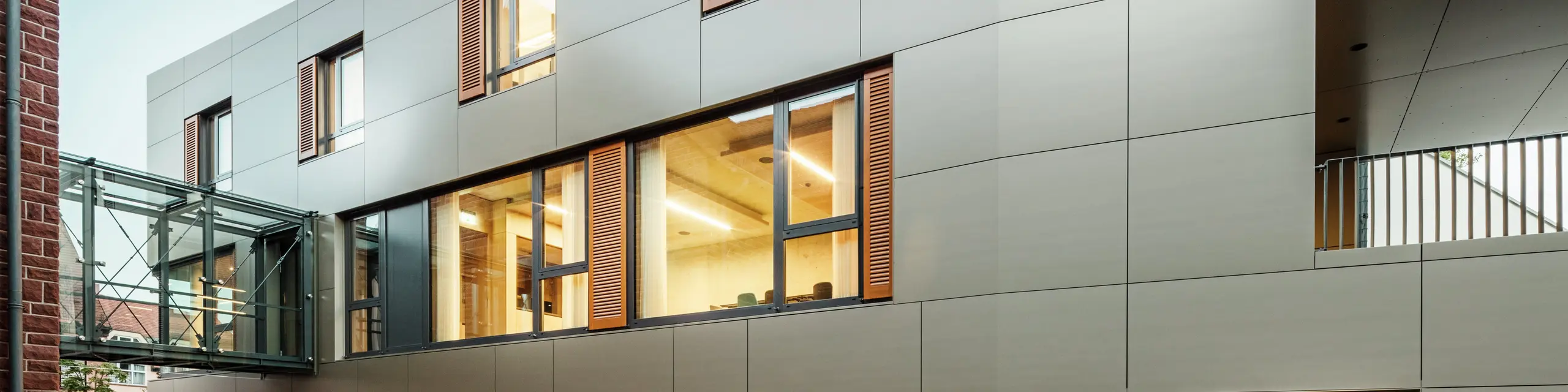 Moderna facciata del municipio di Alzenau, in Germania, con pannelli compositi in alluminio PREFA in bronzo, combinati con persiane e superfici verdi. Il rivestimento in alluminio di alta qualità garantisce un aspetto elegante e duraturo ed è ideale per progetti di costruzione sostenibili. Qui il sito è ben visibile.