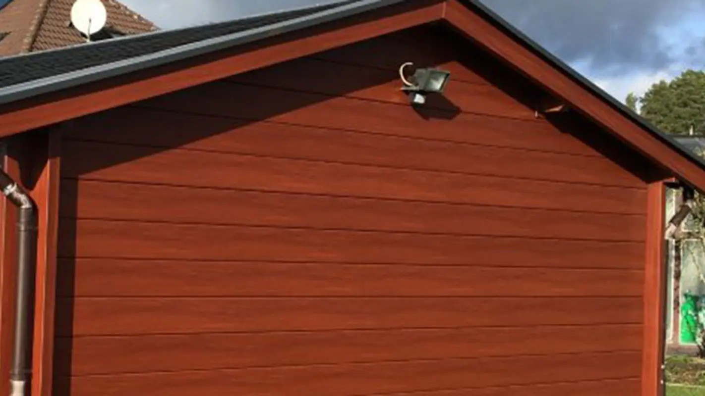 Casetta da giardino ristrutturata, con il nuovo rivestimento delle pareti con effetto legno; prima le pareti erano rivestite in legno, ora con le doghe di rivestimento PREFA nella tonalità legno scuro 