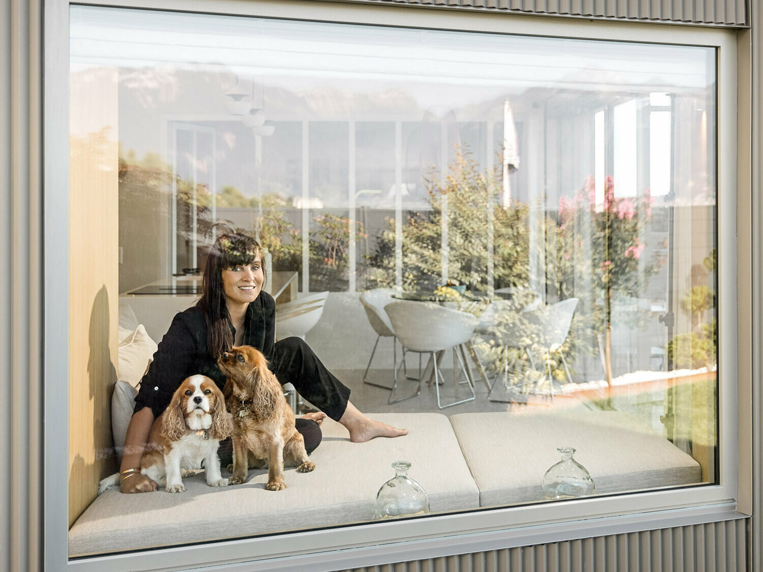 Ritratto fotografico di Sophie Morard seduta con i suoi due cani dietro la finestra nella sua casa sul lago.