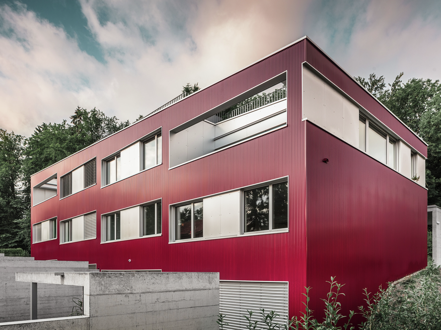 Vista ad angolo dell'edificio residenziale sul Lago di Zurigo in Svizzera, rivestito con il profilo ondulato PREFA nel colore rosso vino