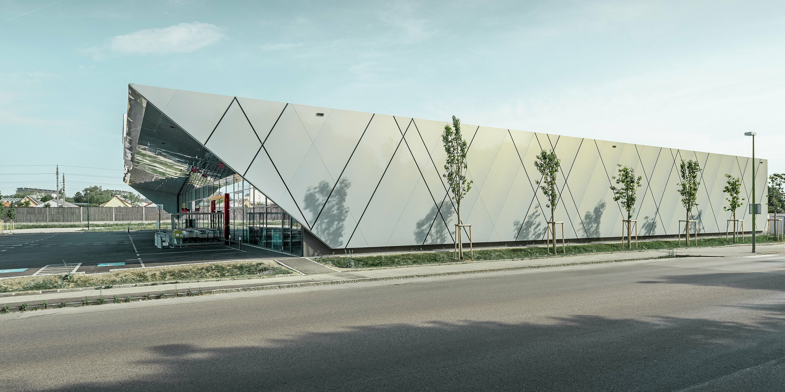 Die Seitenansicht der EUROSPAR Filiale in Wels Gartenstadt zeigt die moderne Fassadengestaltung mit PREFA Aluminium Verbundplatten in der exklusiven Sonderfarbe Silver Gold. Das diagonale Fugenbild verleiht dem Gebäude eine elegante und dynamische Wirkung.
