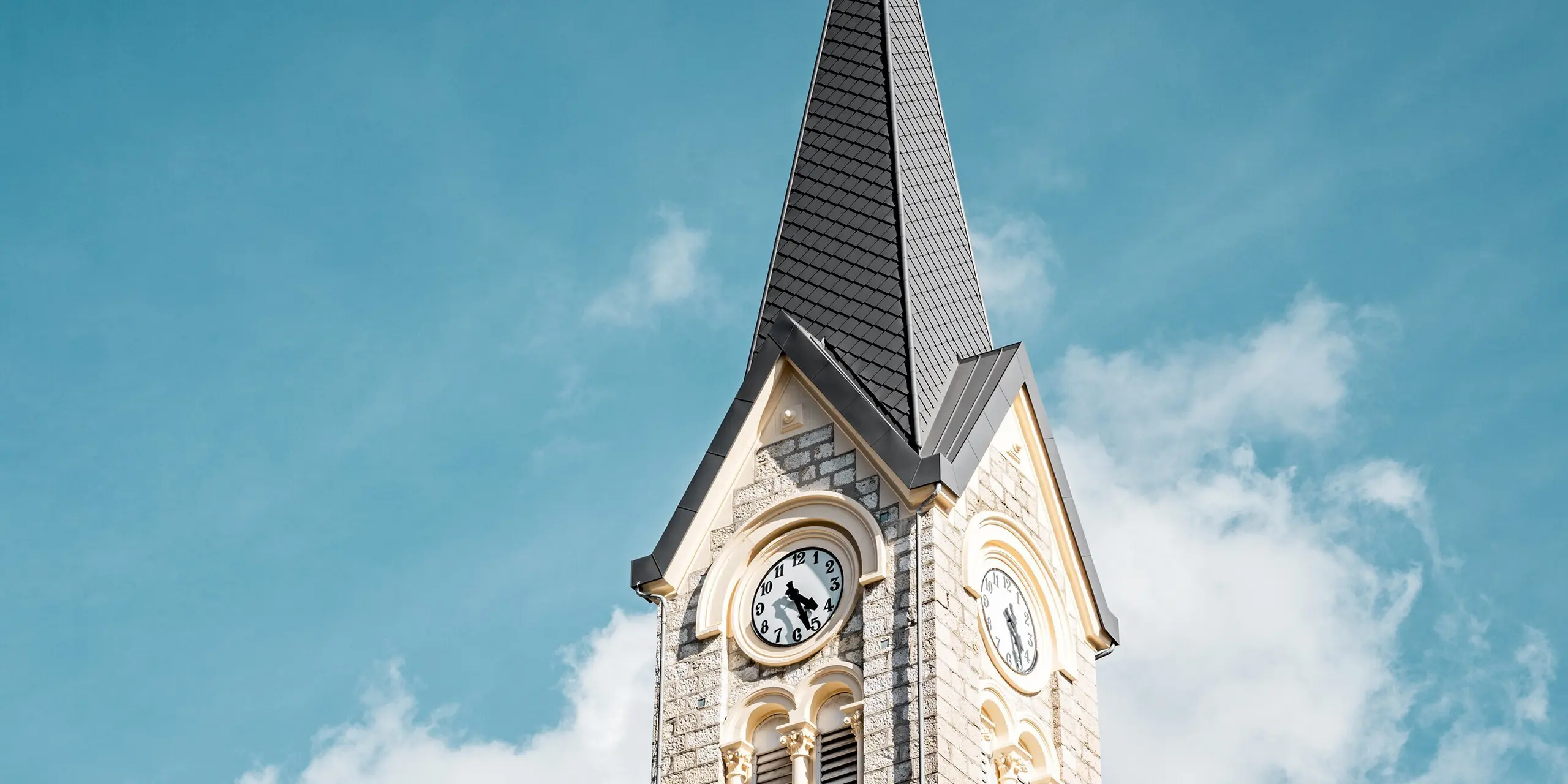 Detailansicht des sanierten Kirchturms in Le Sentier, Schweiz, mit seiner eindrucksvoll aufragenden Turmspitze aus PREFA Dachrauten 29 × 29 in P.10 Dunkelgrau. Die präzise verlegte Aluminiumdeckung betont die elegante Form des Turms und setzt einen markanten Kontrast zum hellen Naturstein. PREFA Aluminium überzeugt durch geringes Gewicht, hohe Witterungsbeständigkeit und langlebigen Schutz für anspruchsvolle Dachkonstruktionen.