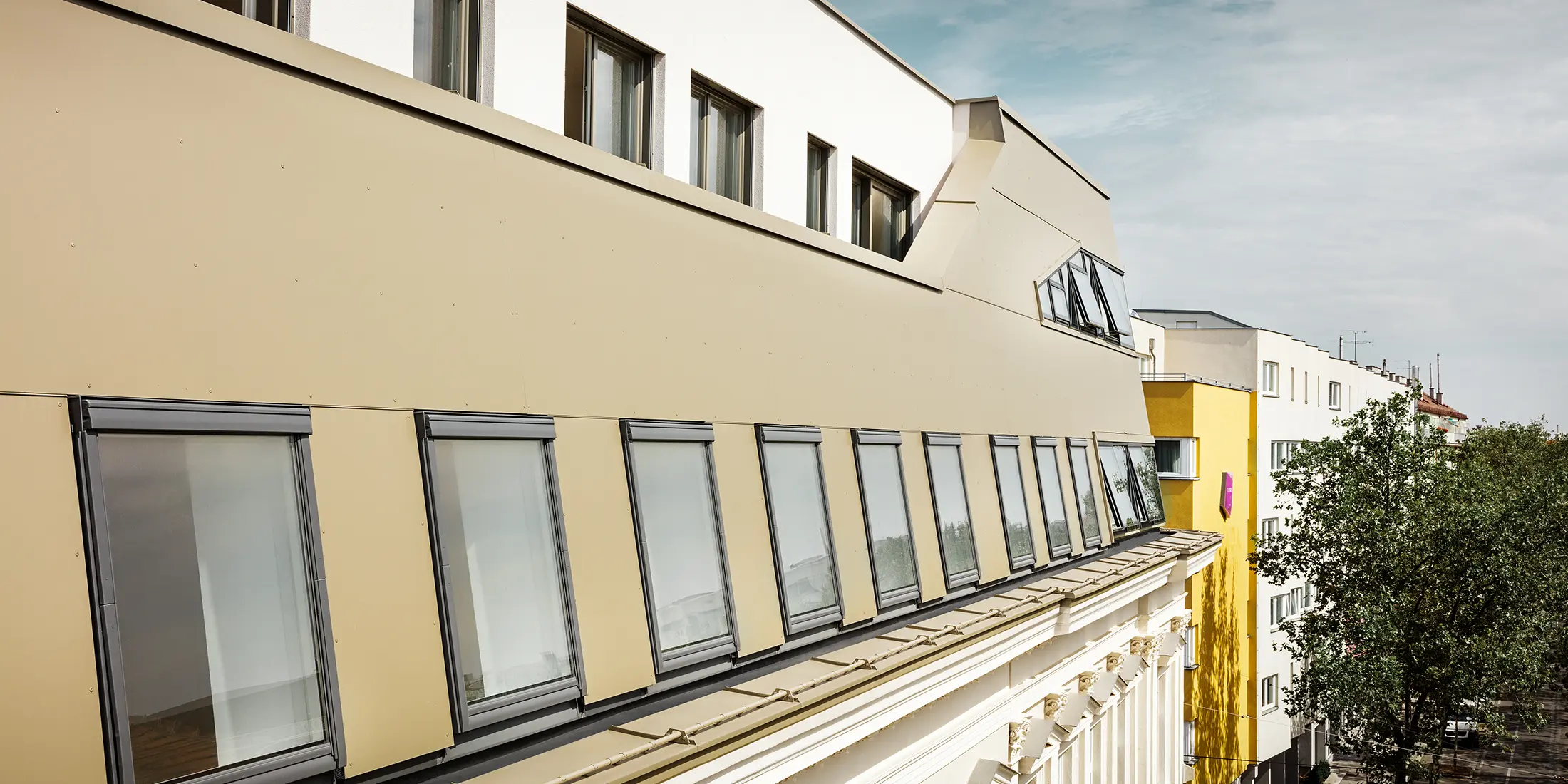 Die seitliche Ansicht des Dachgeschosses hebt die gleichmäßige Verkleidung mit PREFA Aluminium Verbundplatten in Bronze hervor. Große Fenster und flächige Glaselemente sorgen für lichtdurchflutete Räume und ein elegantes, modernes Erscheinungsbild.