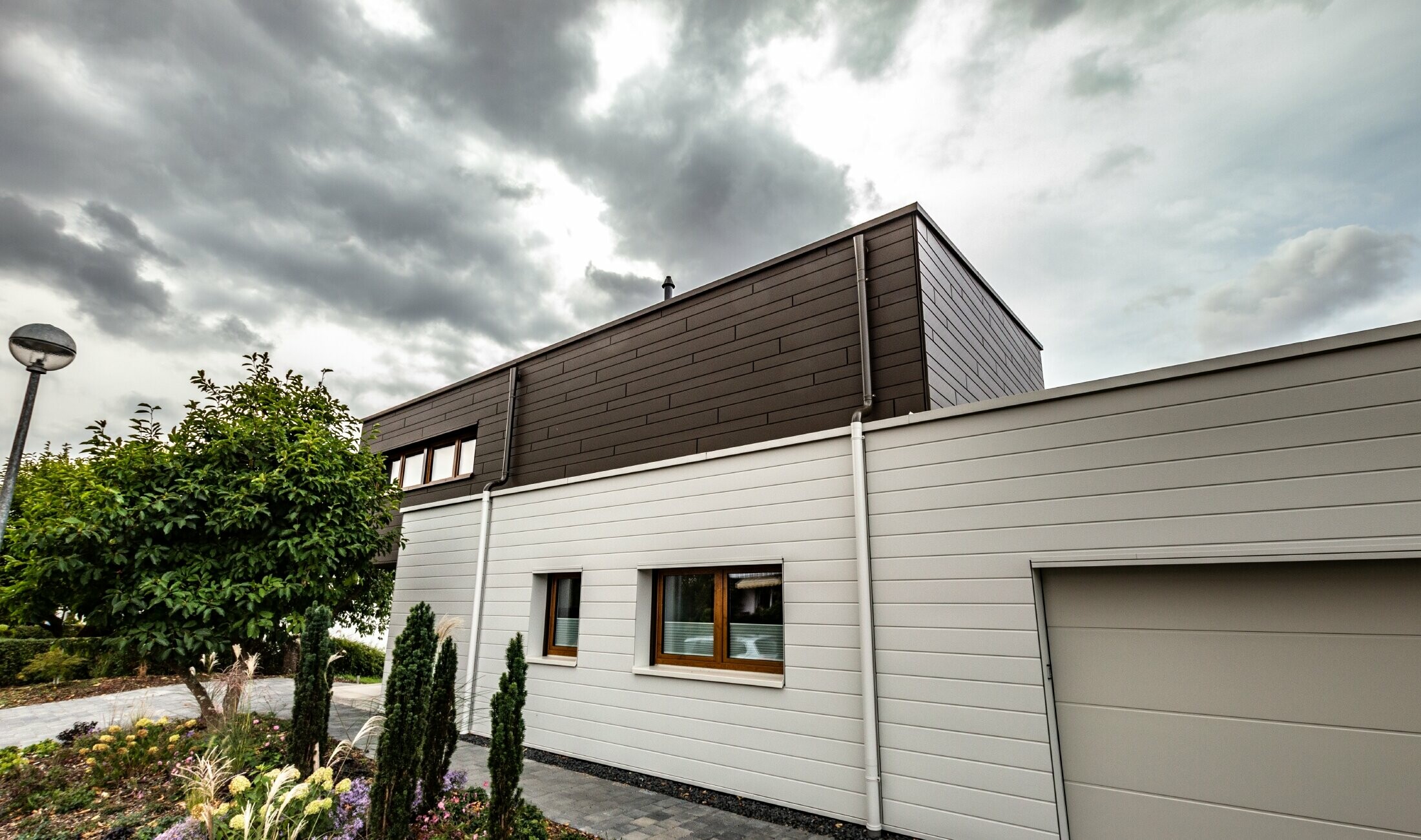 Rivestimento della facciata di un garage con doghe PREFA orizzontali di colore bianco, con grondaia con sbocco.