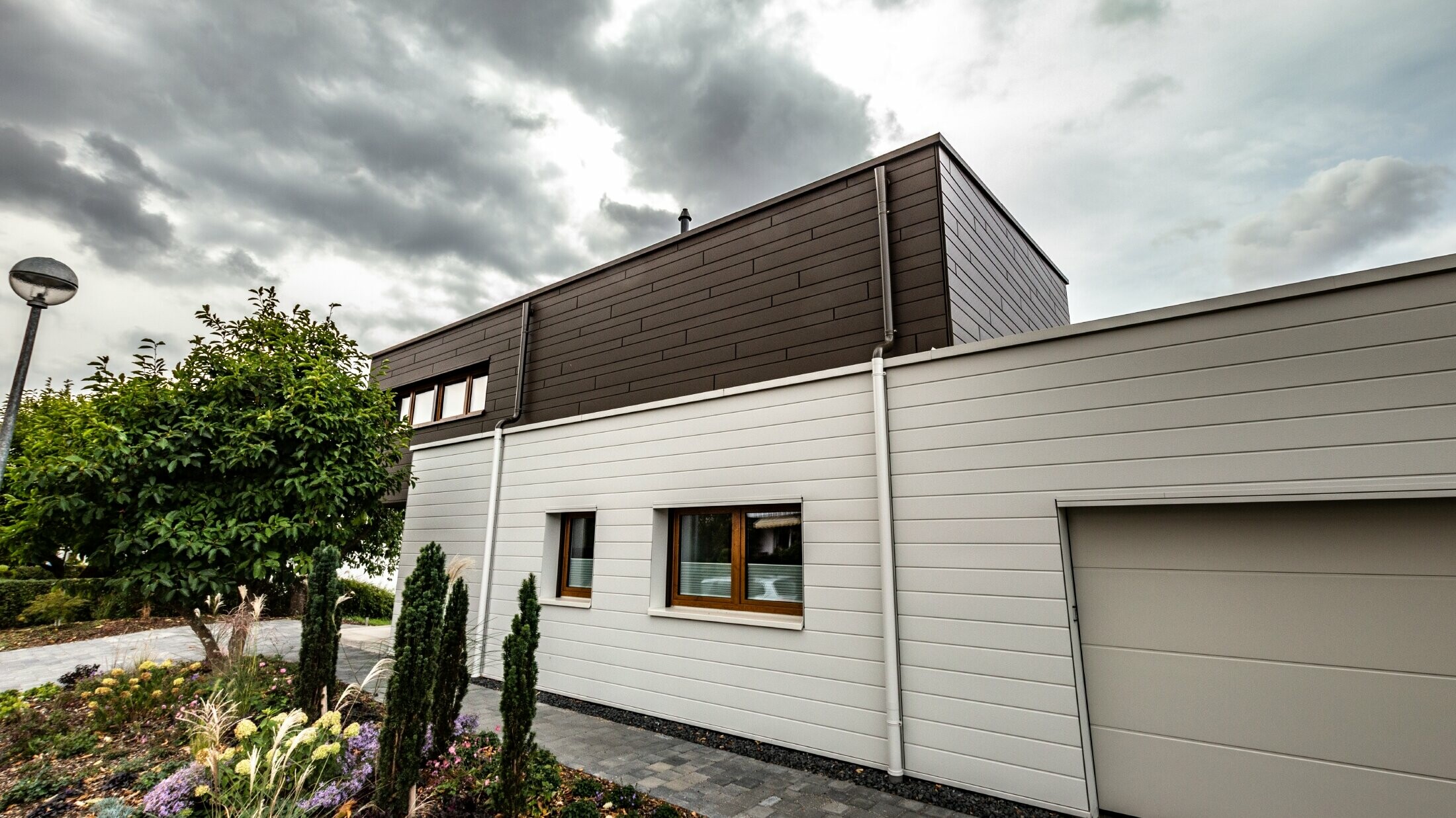 Rivestimento della facciata di un garage con doghe PREFA orizzontali di colore bianco, con grondaia con sbocco.