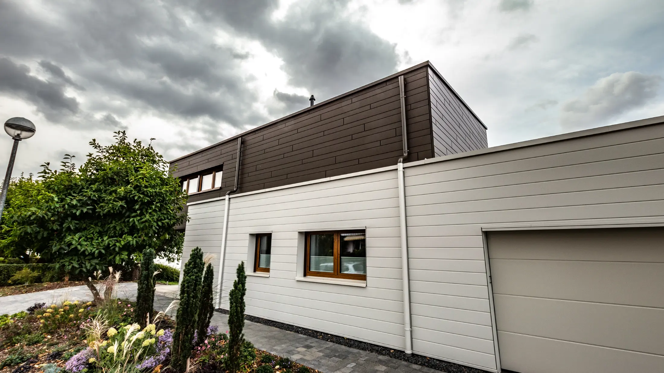 Rivestimento della facciata di un garage con doghe PREFA orizzontali di colore bianco, con grondaia con sbocco.