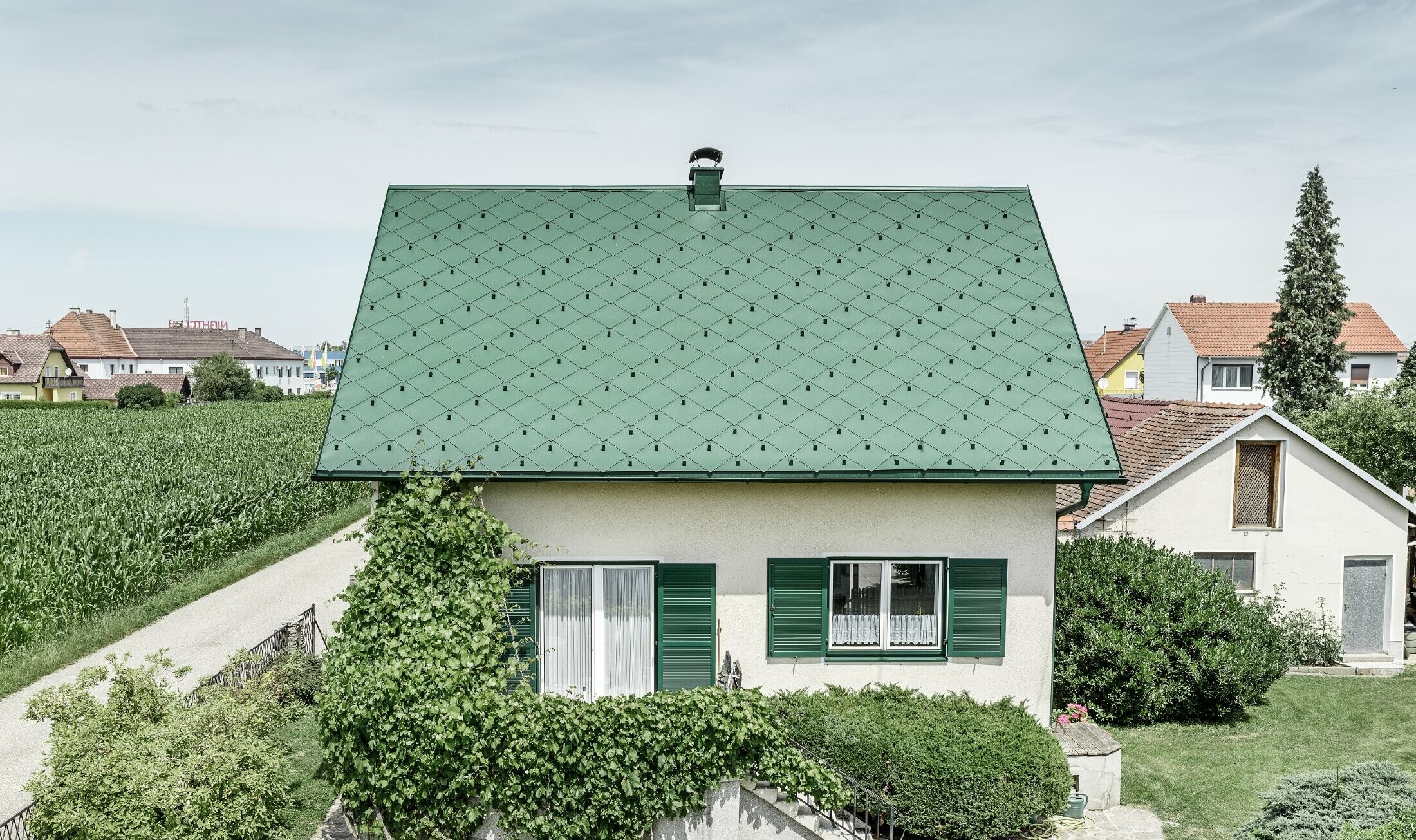 Casa unifamiliare classica con tetto a due falde con copertura in alluminio di colore verde muschio e  persiane verdi. Il tetto è stato coperto con scaglie PREFA 44 × 44 in P.10 verde muschio.