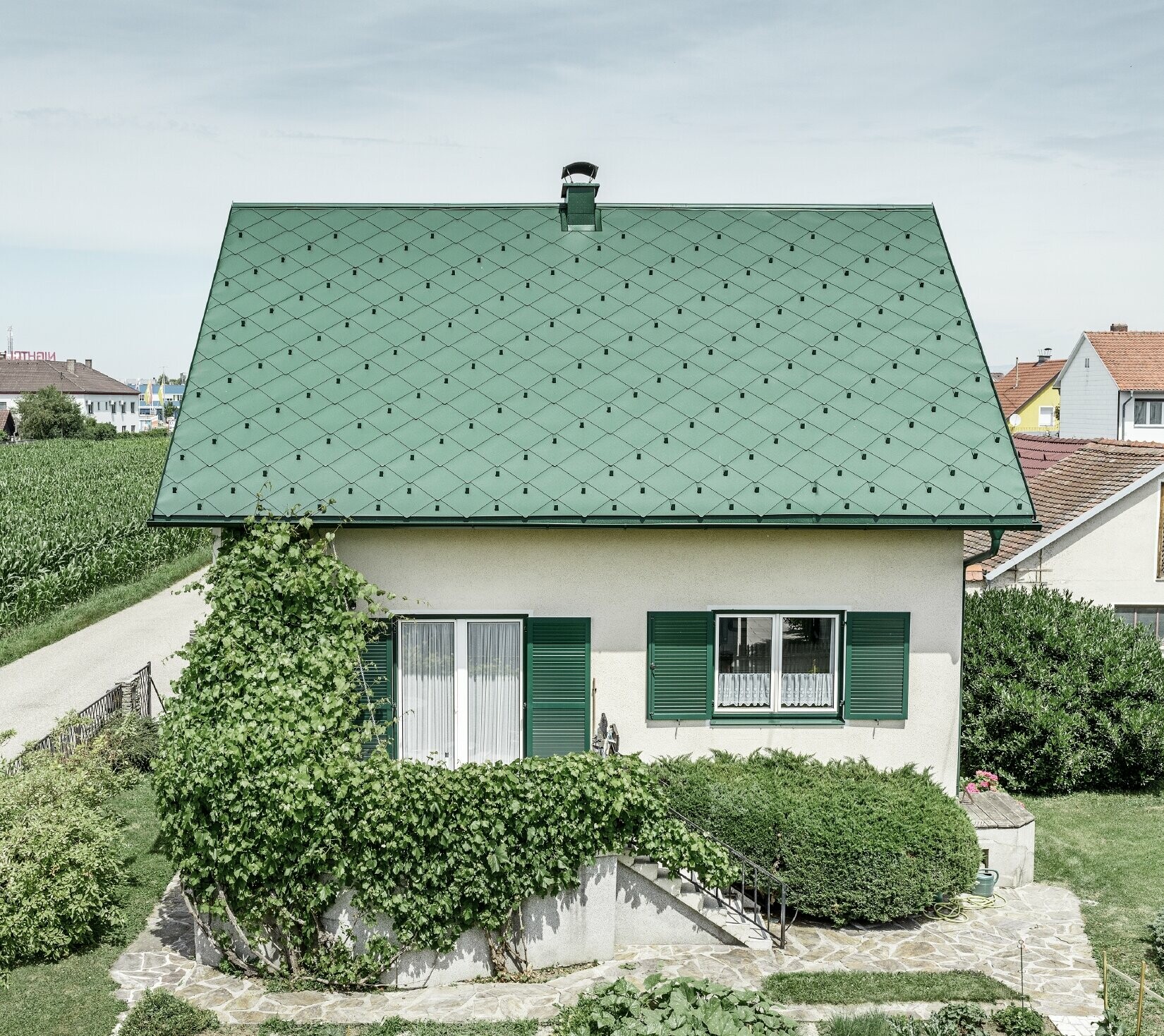 Casa unifamiliare classica con tetto a due falde con copertura in alluminio di colore verde muschio e  persiane verdi. Il tetto è stato coperto con scaglie PREFA 44 × 44 in P.10 verde muschio.
