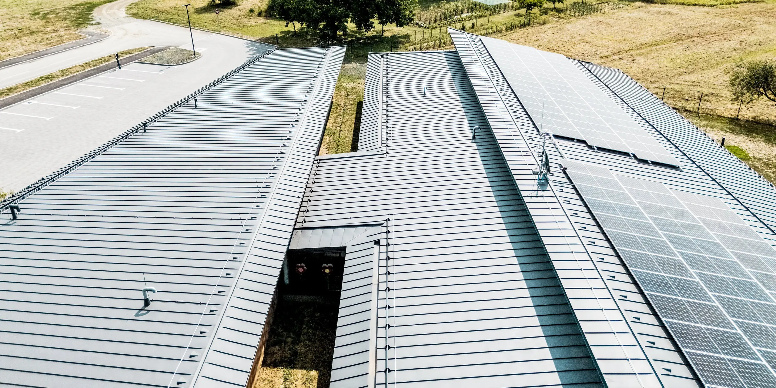 Drohnenperspektive auf die weitläufige PREFALZ Dachlandschaft des Kindergartens Svarozic in Kroatien. Die anthrazitfarbene Aluminiumdeckung mit präzisen Stehfalzen, integrierter Photovoltaikanlage und klarer Geometrie prägt das moderne Gebäude. PREFA Aluminium verbindet geringes Gewicht, langlebige Qualität und zuverlässigen Witterungsschutz mit einer zeitgemäßen, nachhaltigen Architektur.