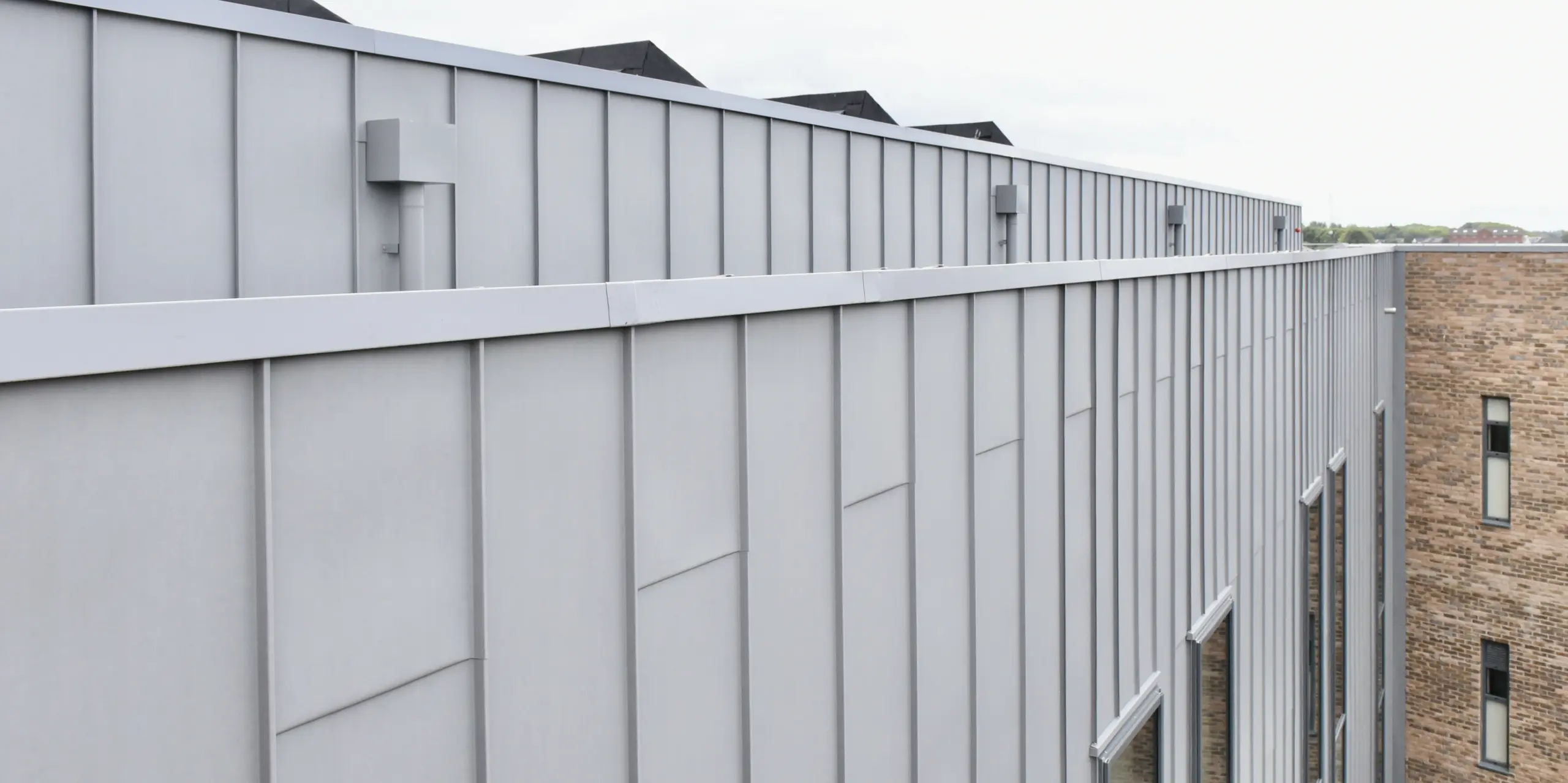 Detailansicht der PREFALZ Aluminiumfassade in Patinagrau am Regional College North, UK. Die klare Linienführung und die matte Optik der Stehfalzverkleidung unterstreichen die hochwertige Verarbeitung und das zeitlose Design.