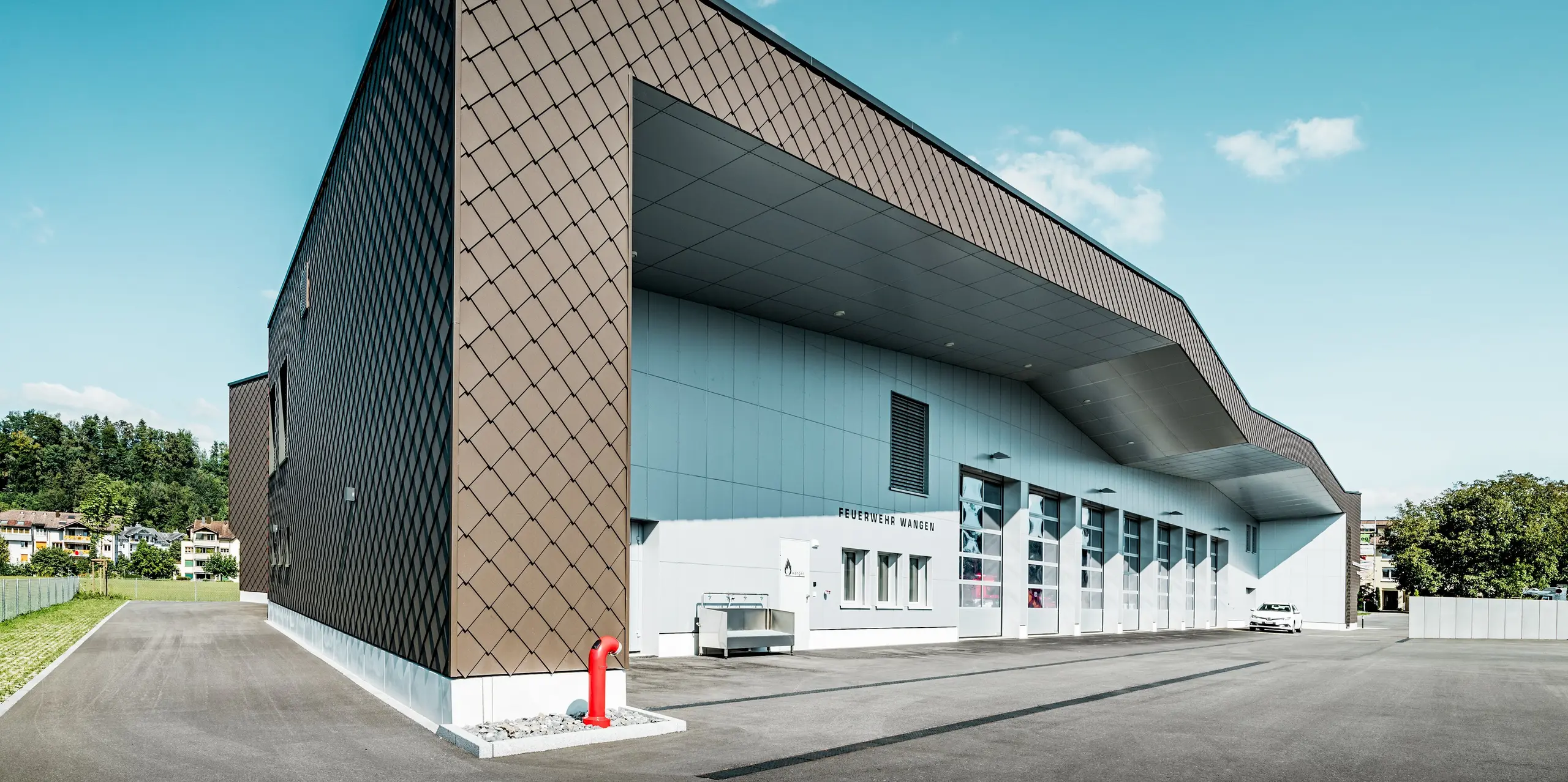 Beeindruckende Gesamtansicht der Feuerwehr und des Elektrizitätswerks in Wangen, Schweiz. Die großflächige Fassade aus PREFA Wandrauten 29 × 29 in P.10 Braun schafft mit ihrer markanten Rautenstruktur eine außergewöhnliche Tiefenwirkung. Aluminium Verbundplatten in P.10 Prefaweiß setzen moderne Kontraste. Die langlebigen PREFA Aluminiumprodukte verbinden anspruchsvolle Architektur mit hoher Witterungsbeständigkeit, geringer Wartung und nachhaltiger Wertbeständigkeit.