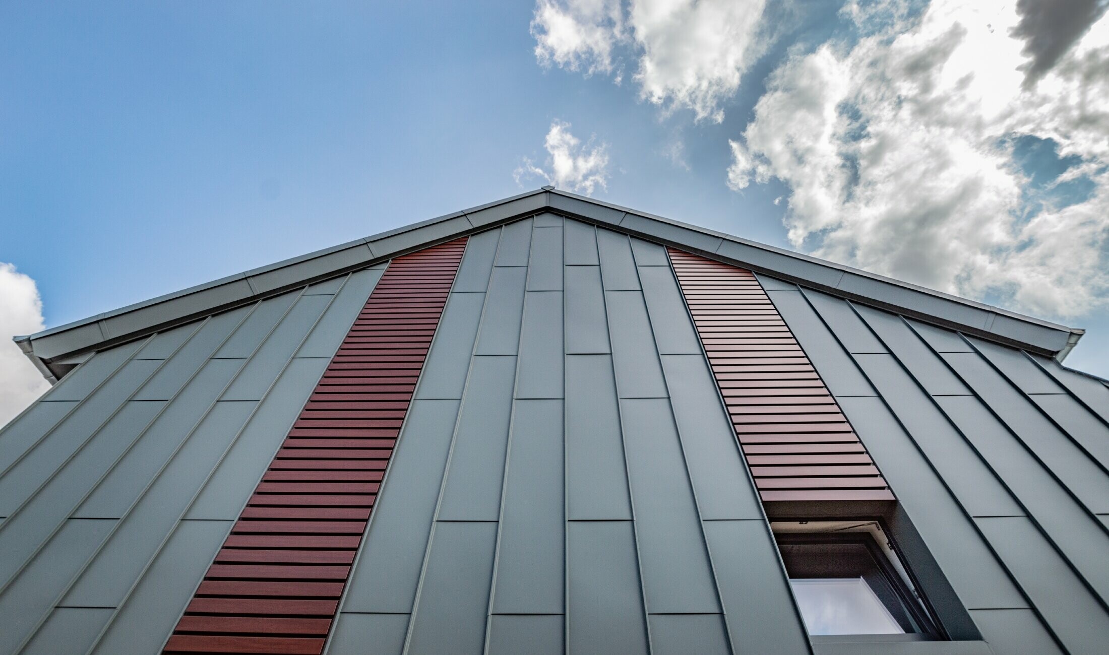 Facciata ad aggraffatura angolare verticale con copertura a lastre in grigio chiaro, con doga orizzontale in legno scuro di PREFA.