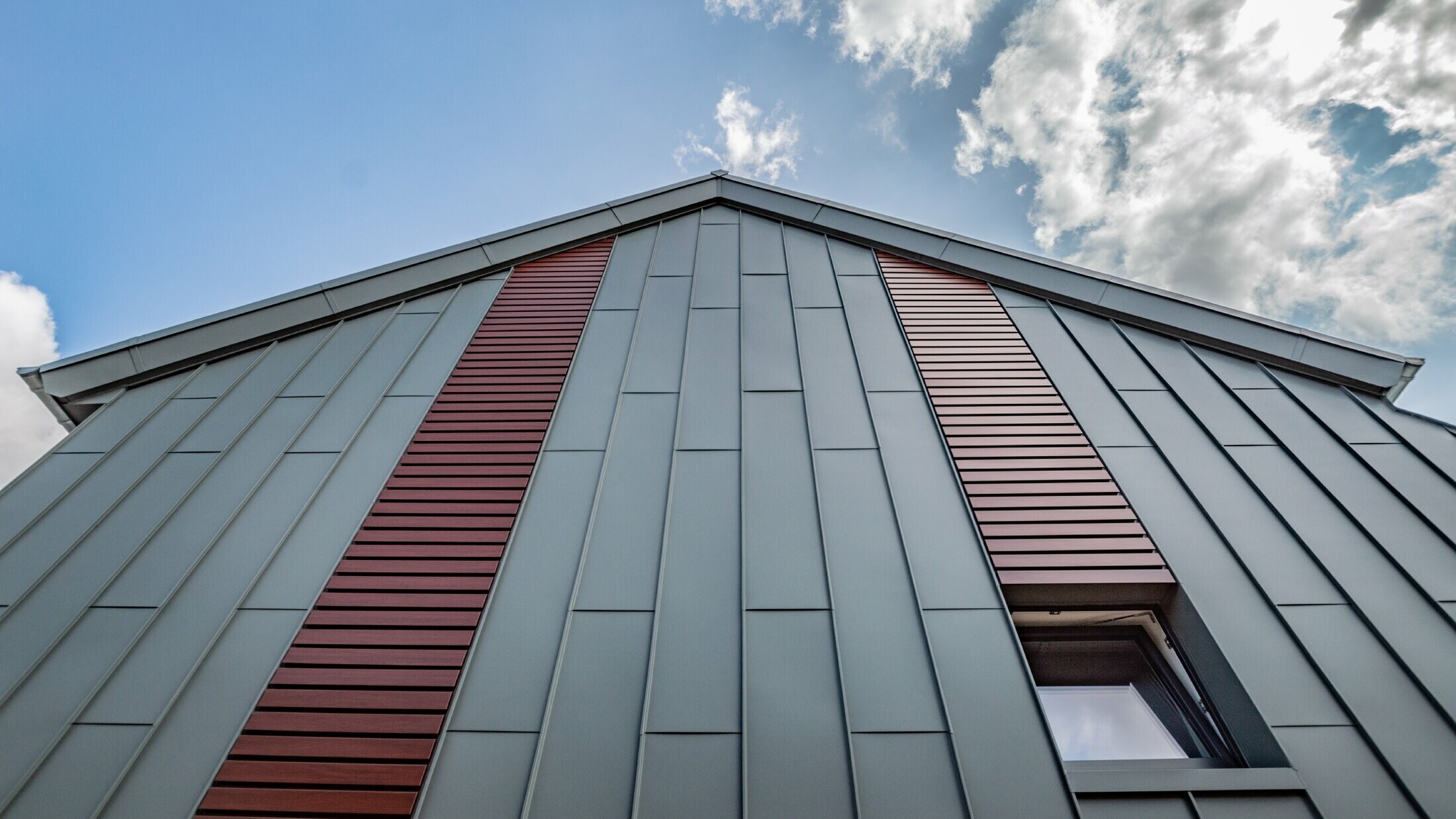 Facciata ad aggraffatura angolare verticale con copertura a lastre in grigio chiaro, con doga orizzontale in legno scuro di PREFA.