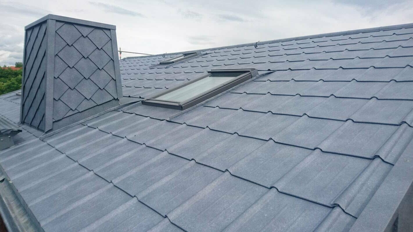 Immagine dettagliata di un tetto ristrutturato con tegole PREFA colore P.10 grigio pietra, incluso rivestimento del camino