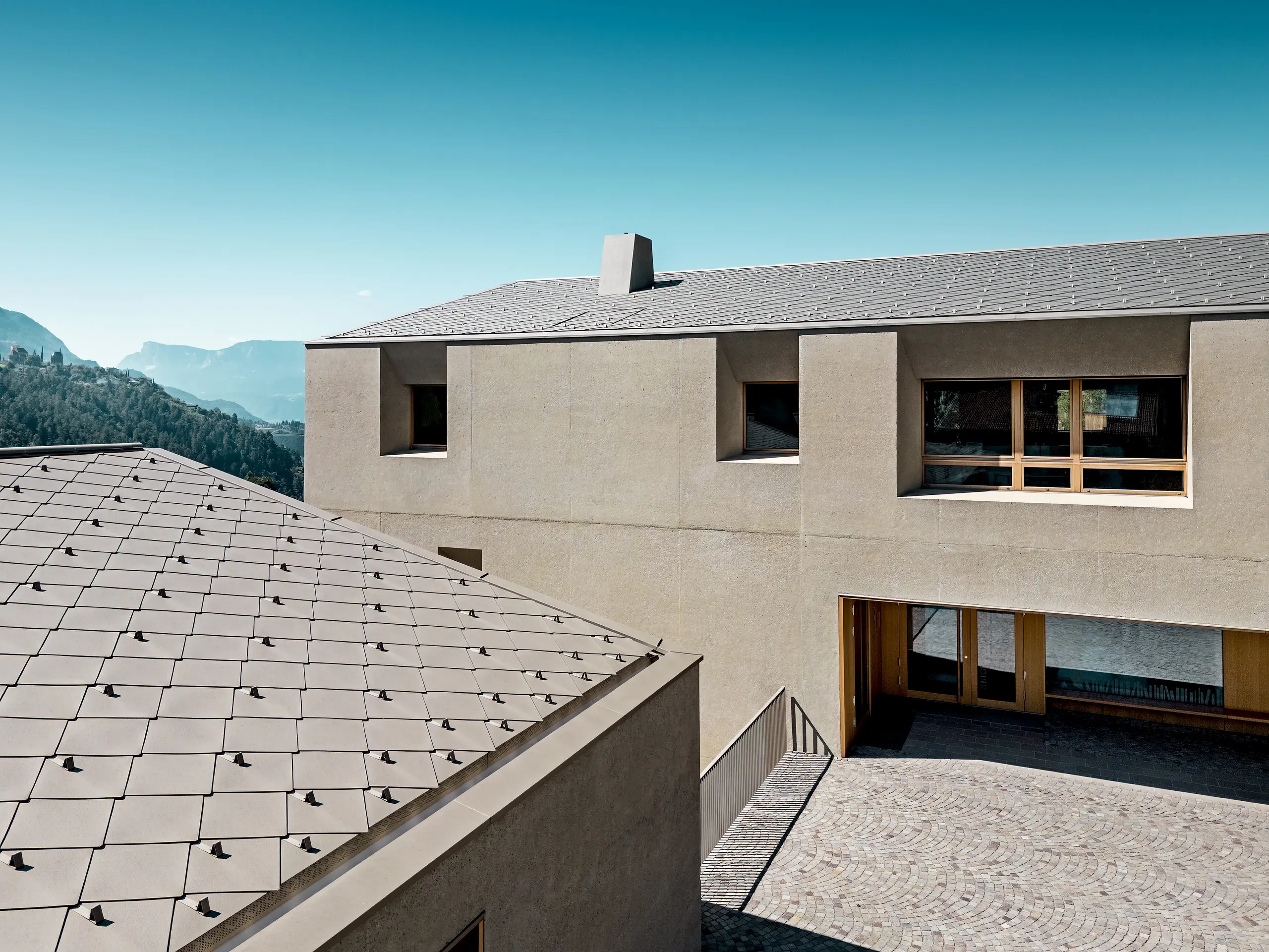 Vista dettagliata del centro di formazione di Riffian con le scaglie 44 × 44 PREFA nella finitura P.10 bronze. La copertura in alluminio, posata con precisione sugli edifici dalle linee pulite, sottolinea l’architettura moderna, offre una protezione duratura dagli agenti atmosferici e si integra armoniosamente con il naturale scenario montano altoatesino.