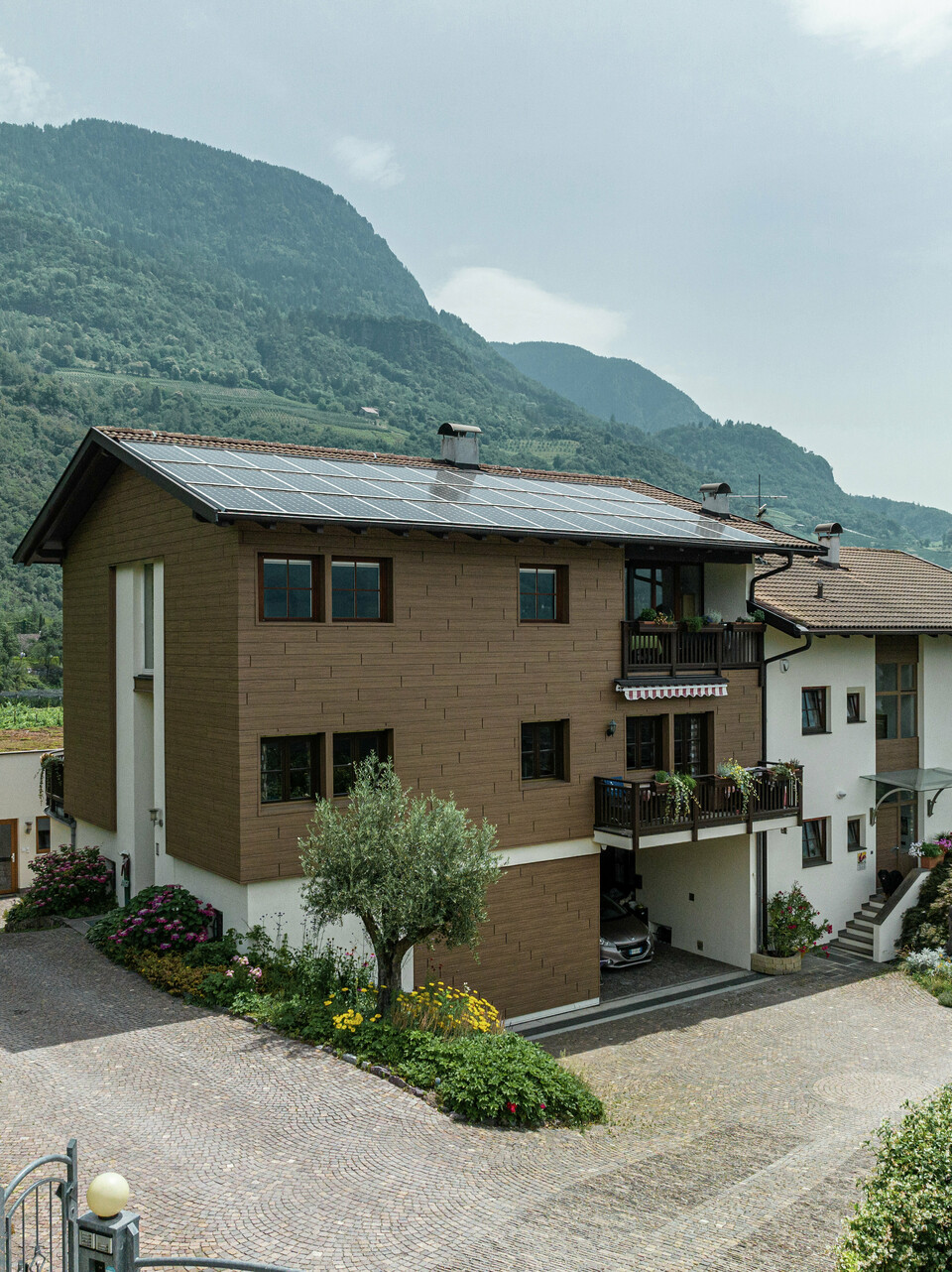 Sanierte Ferienwohnungen Prechtlhof in Meran, Südtirol, mit PREFA Sidings in Walnussbraun und einer Photovoltaikanlage am Dach. Die langlebige Aluminiumfassade in Holzoptik sorgt für natürliche Ästhetik, höchste Widerstandsfähigkeit und geringen Wartungsaufwand, ideal für die alpine Umgebung.