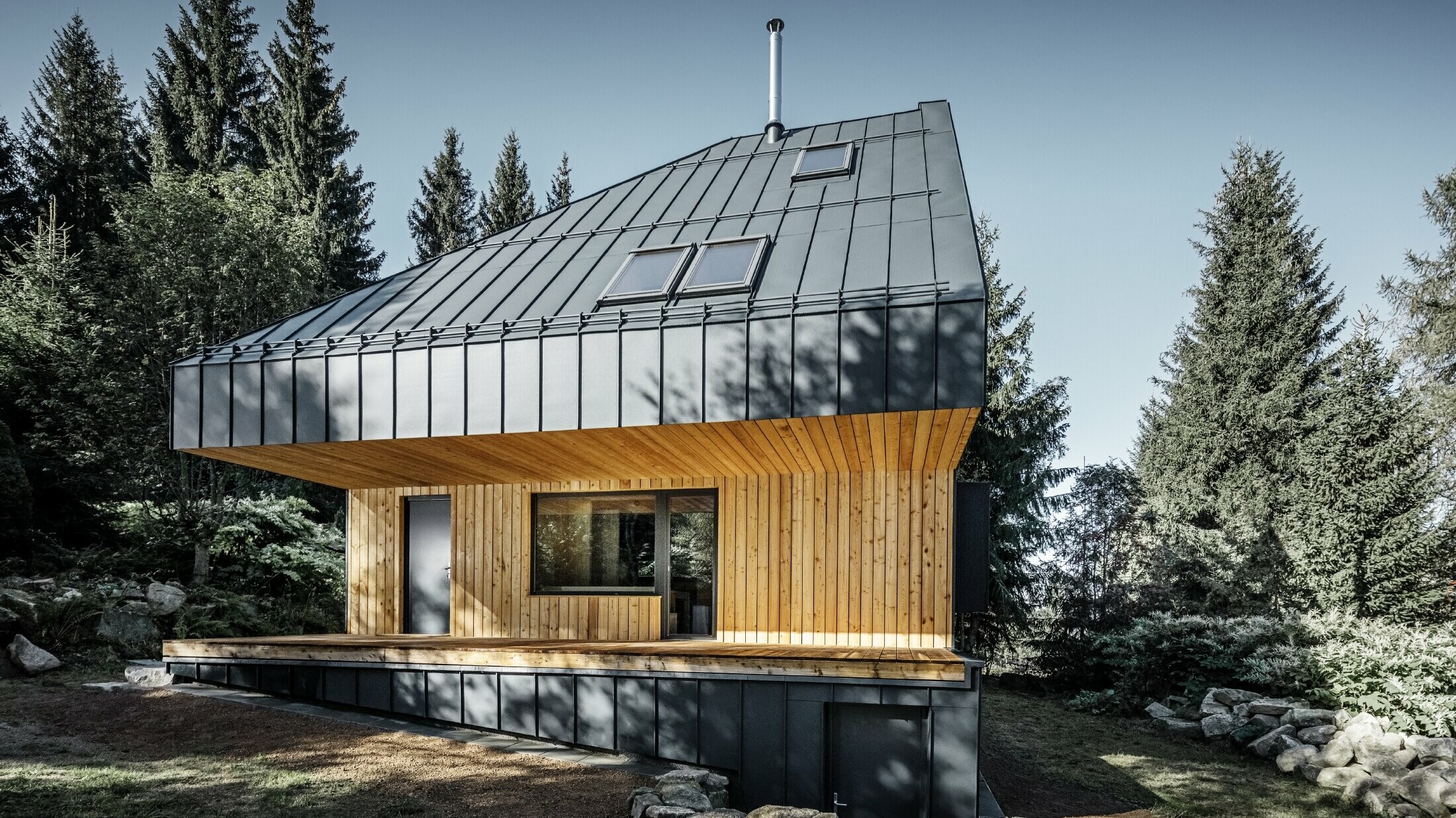 Casa unifamiliare moderna nel bosco, l'imponente tetto è stato rivestito con Prefalz in alluminio di PREFA in antracite. La vista dal basso e la facciata sono rivestite con pannelli di legno.