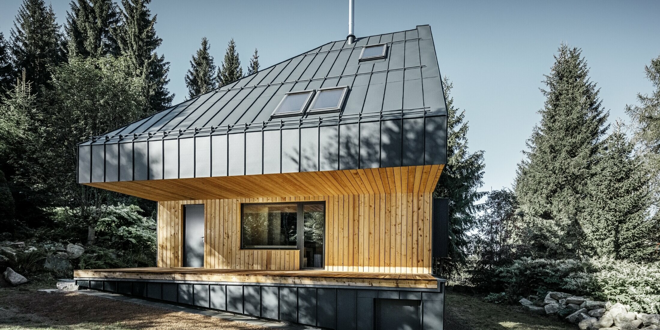 Casa unifamiliare moderna nel bosco, l'imponente tetto è stato rivestito con Prefalz in alluminio di PREFA in antracite. La vista dal basso e la facciata sono rivestite con pannelli di legno.