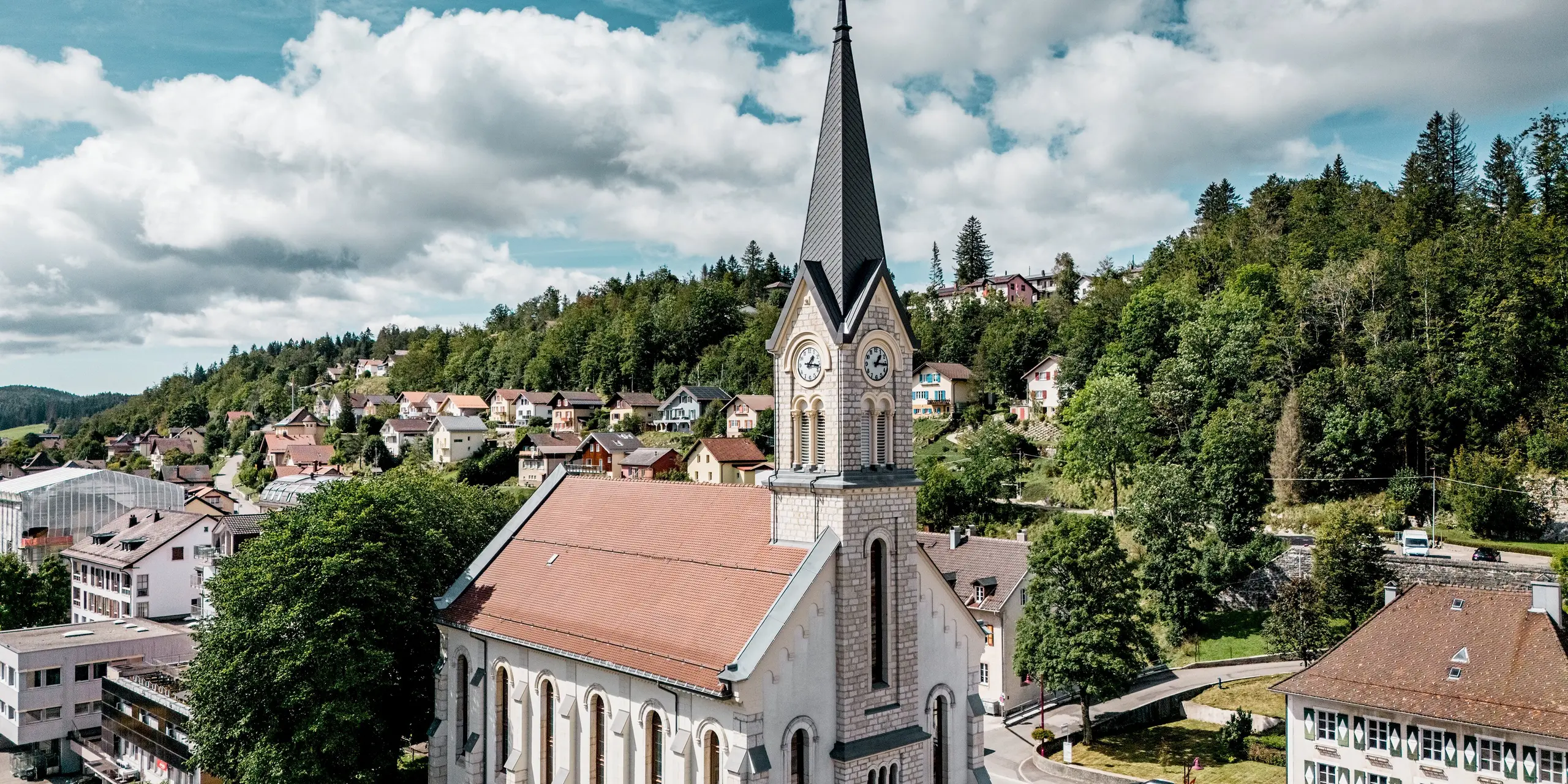 Historische Kirche in Le Sentier, Schweiz, mit markanter Turmspitze aus PREFA Dachrauten 29 × 29 in P.10 Dunkelgrau. Die robuste Aluminiumdeckung setzt einen spannenden Kontrast zum hellen Naturstein und prägt das Ortsbild eindrucksvoll. PREFA Aluminium überzeugt durch Langlebigkeit, geringes Gewicht und hohe Widerstandsfähigkeit bei anspruchsvollen Dachgeometrien.