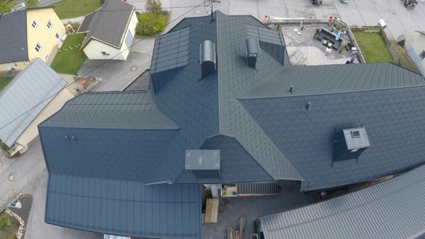 Ristrutturazione di un tetto ad ampia superficie con molti dettagli - compluvi, abbaini e camini. Il tetto è stato coperto con tegole R.16 PREFA in alluminio color antracite.