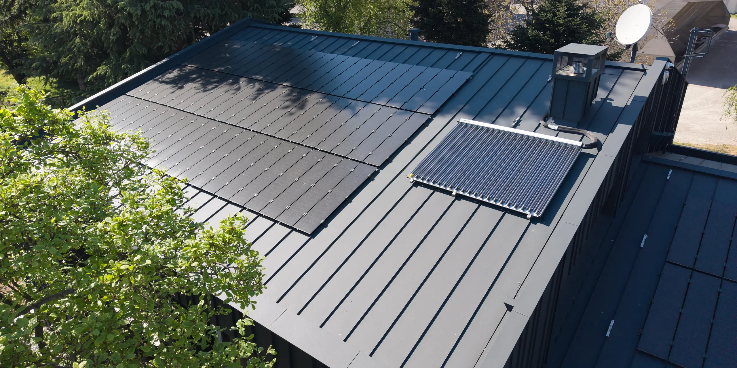 Luftaufnahme des modernen PREFALZ Aluminiumdachs der Villa Castellanza in P.10 Anthrazit. Die nahtlos integrierten PREFALZ Solarmodule bilden den zentralen Blickfang und verbinden ästhetisches Design mit nachhaltiger Energiegewinnung. Klare Stehfalzlinien, langlebige PREFA Qualität und die Einbettung in die grüne Umgebung schaffen ein beeindruckendes architektonisches Gesamtbild.