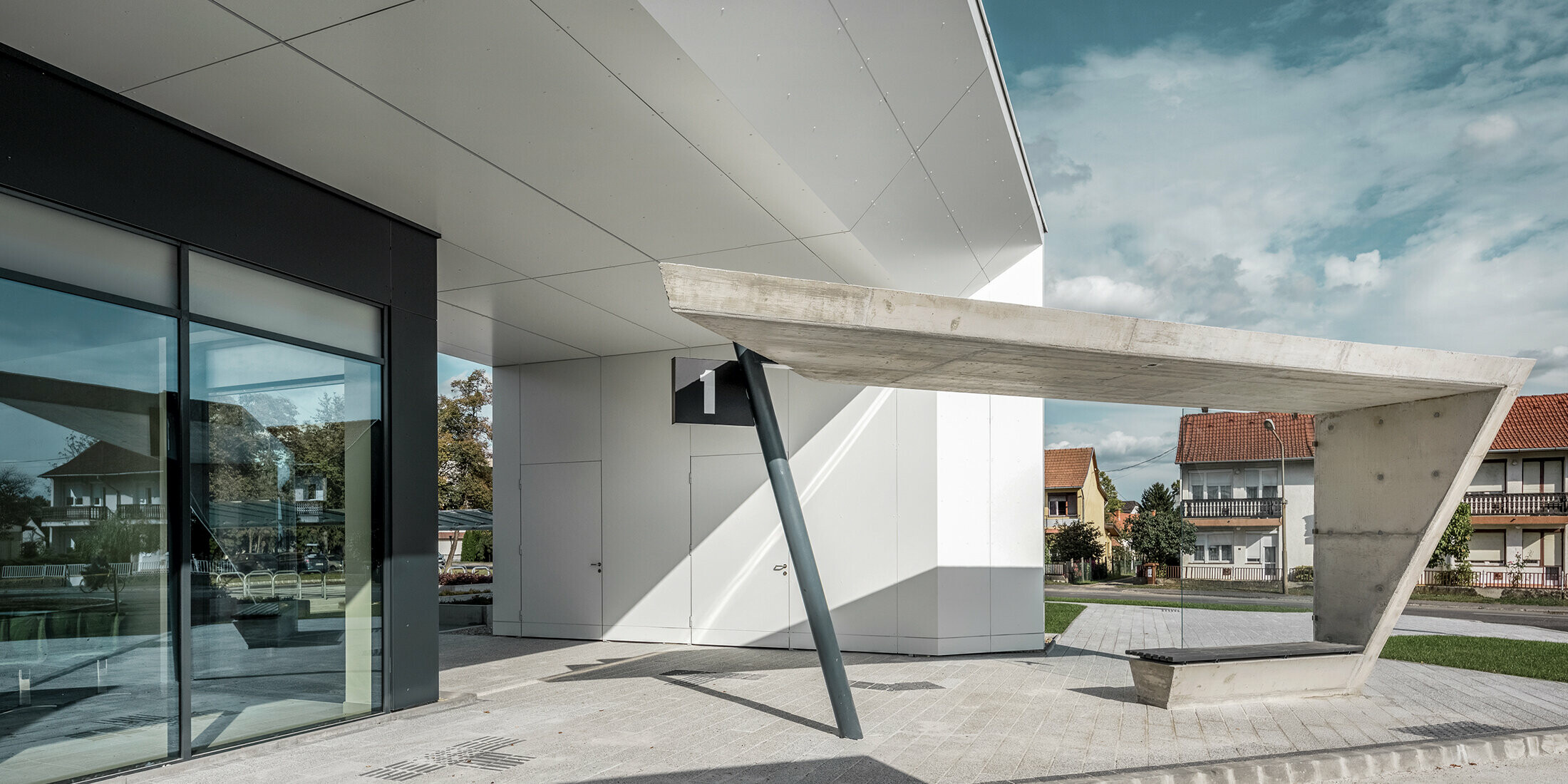 Eingangsbereich des Busbahnhofs Lenti; die Untersicht der Überdachung ist mit der PREFABOND Aluminium Verbundplatte von PREFA in Reinweiß verkleidet, die Fassadenelemente bei den Eingangstüren und Schaufenstern ist in P.10 anthrazit verkleidet.