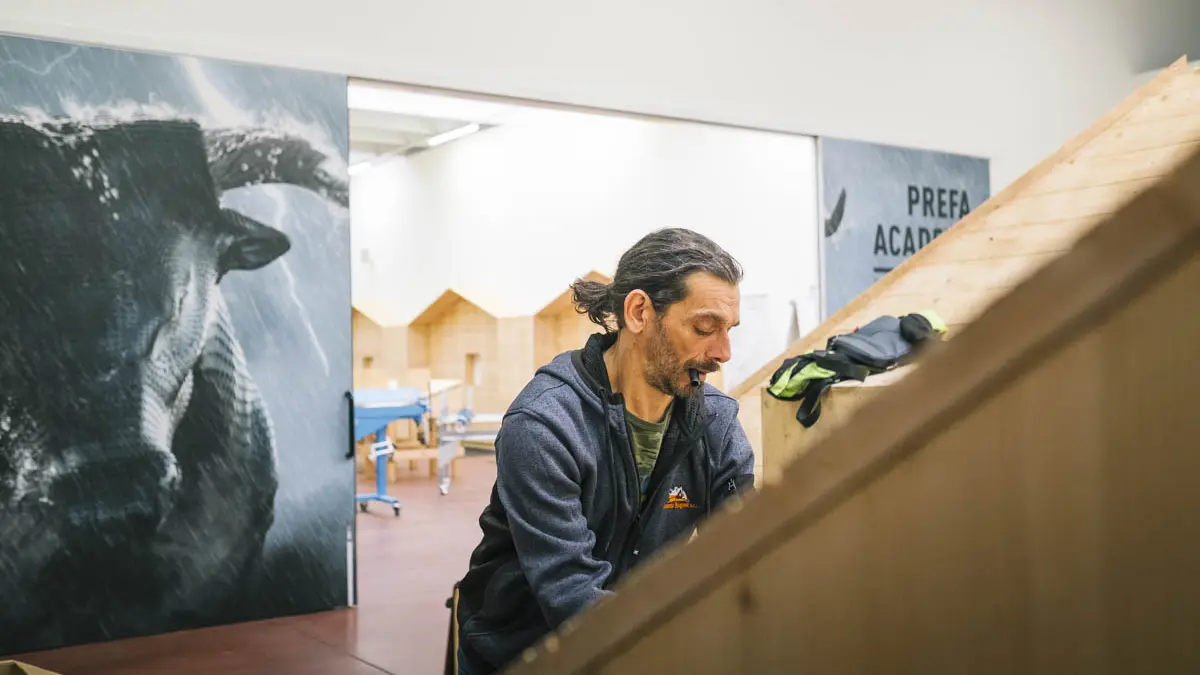 Ein Teilnehmer der PREFA Academy Italien arbeitet konzentriert an einem Schulungsmodell mit Holzunterkonstruktion, an dem er ein PREFA Dachprodukt montiert. 