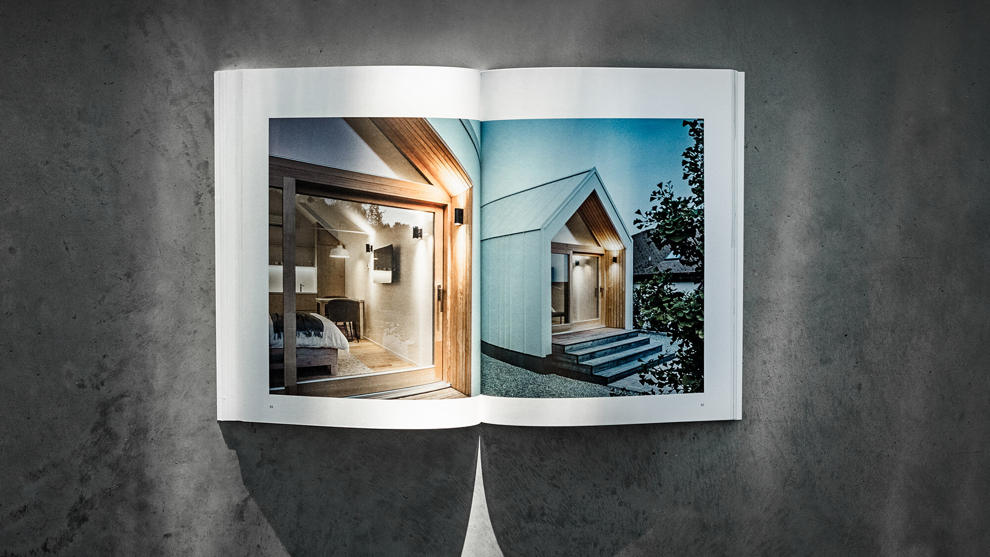 Libro PREFARENZEN 2024 aperto, su sfondo grigio, con due pagine su cui sono raffigurate le case modulari di kubico domino arhitekti.